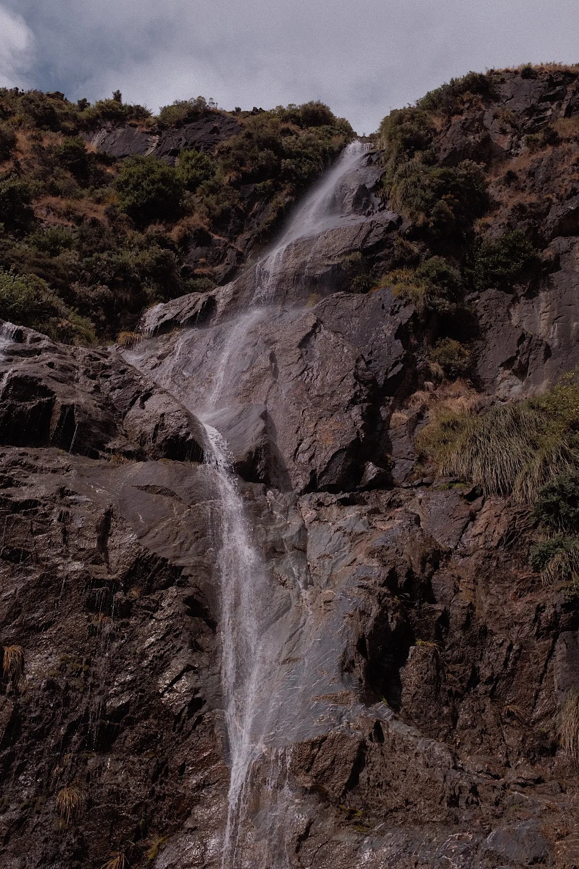Small waterfall on rocky cliff with greenery