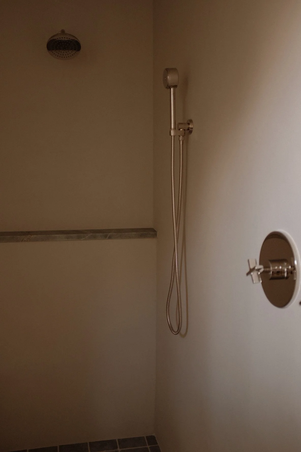 An empty shower area with a handheld showerhead, a small mirror attached to a wall, and a ledge with a marble edge.