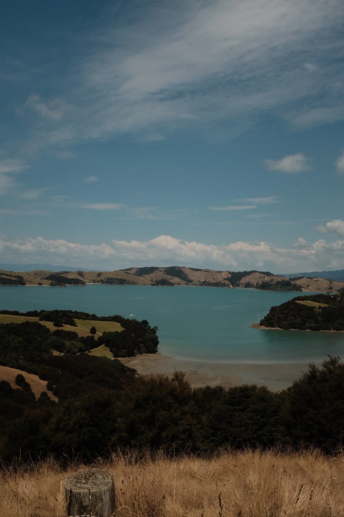 Tranquil lake surrounded by trees and distant hills under a partly cloudy sky.