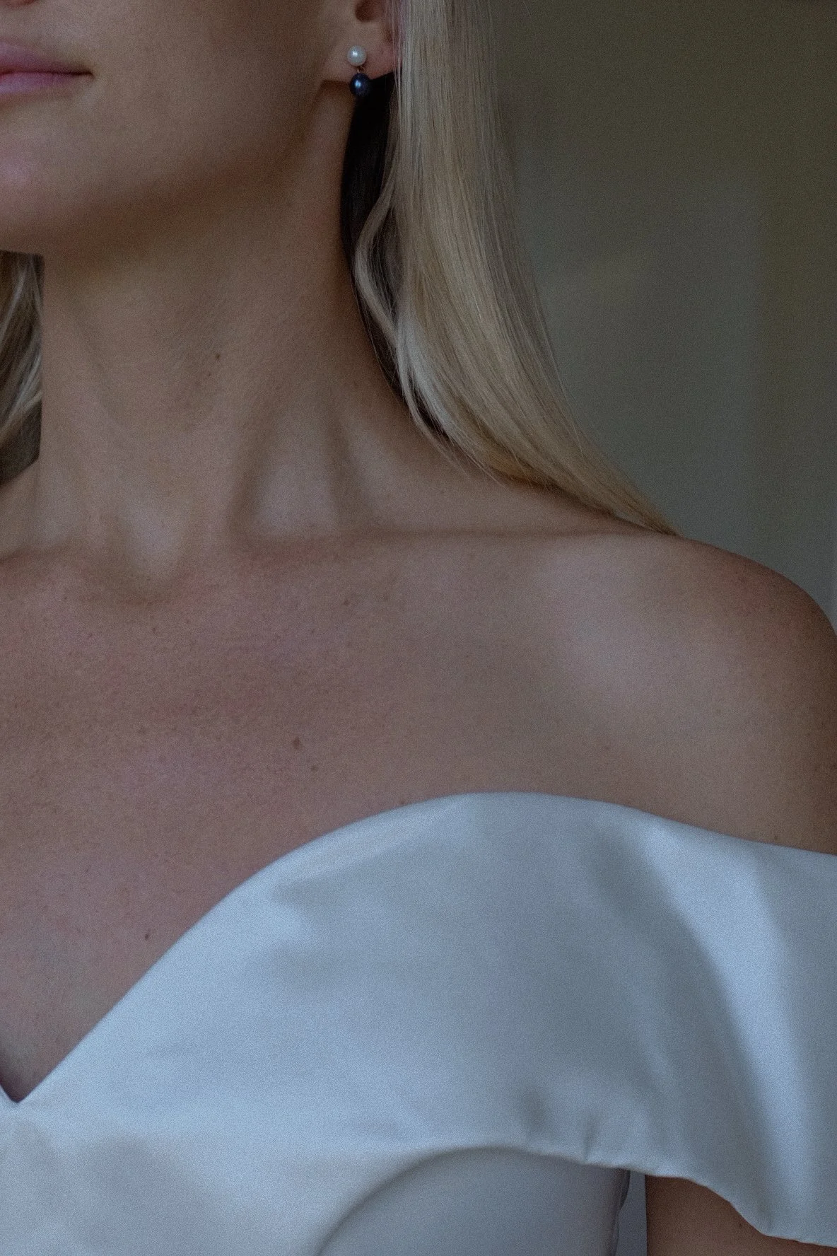 Close-up of a woman wearing a white off-the-shoulder dress and pearl earrings, blonde hair visible.