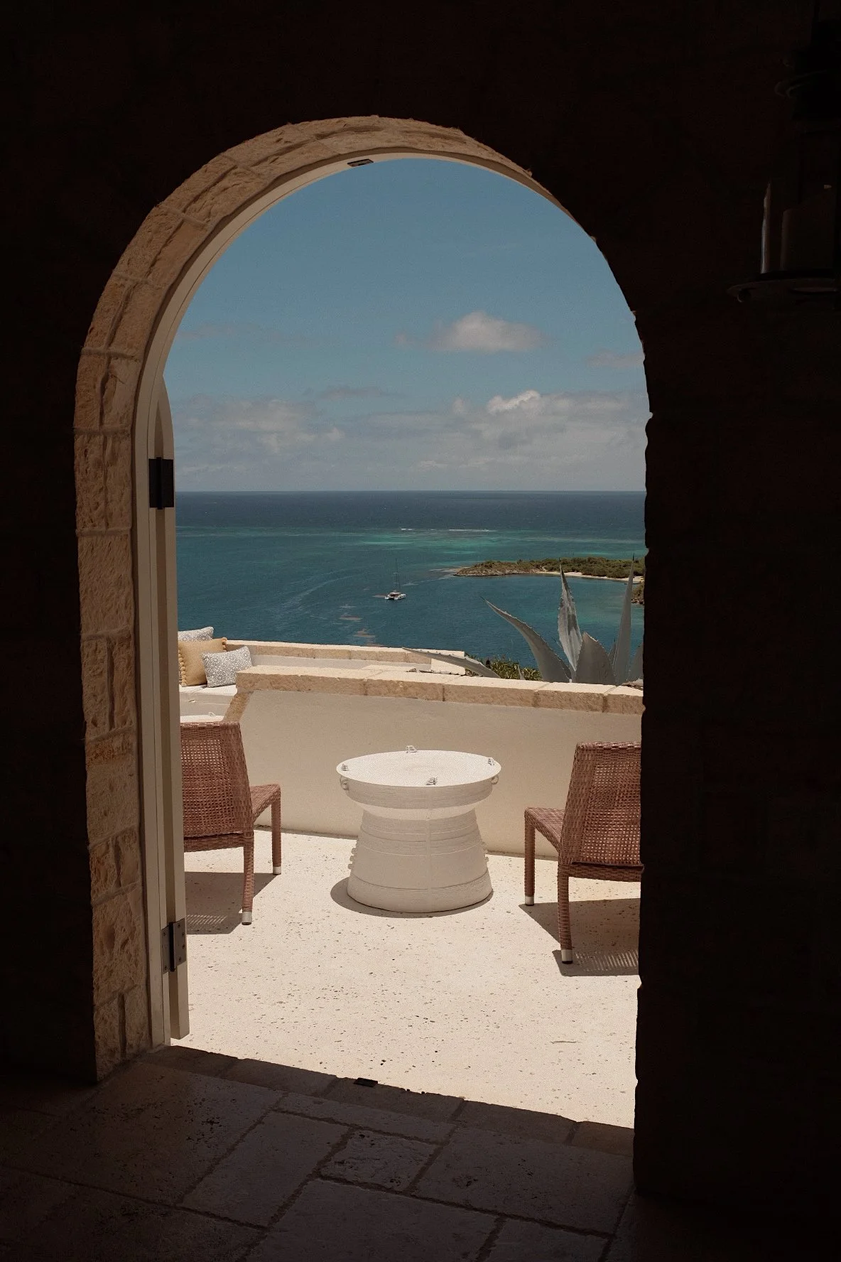 Archway leading to a patio with two wicker chairs and a small round table overlooking the ocean.