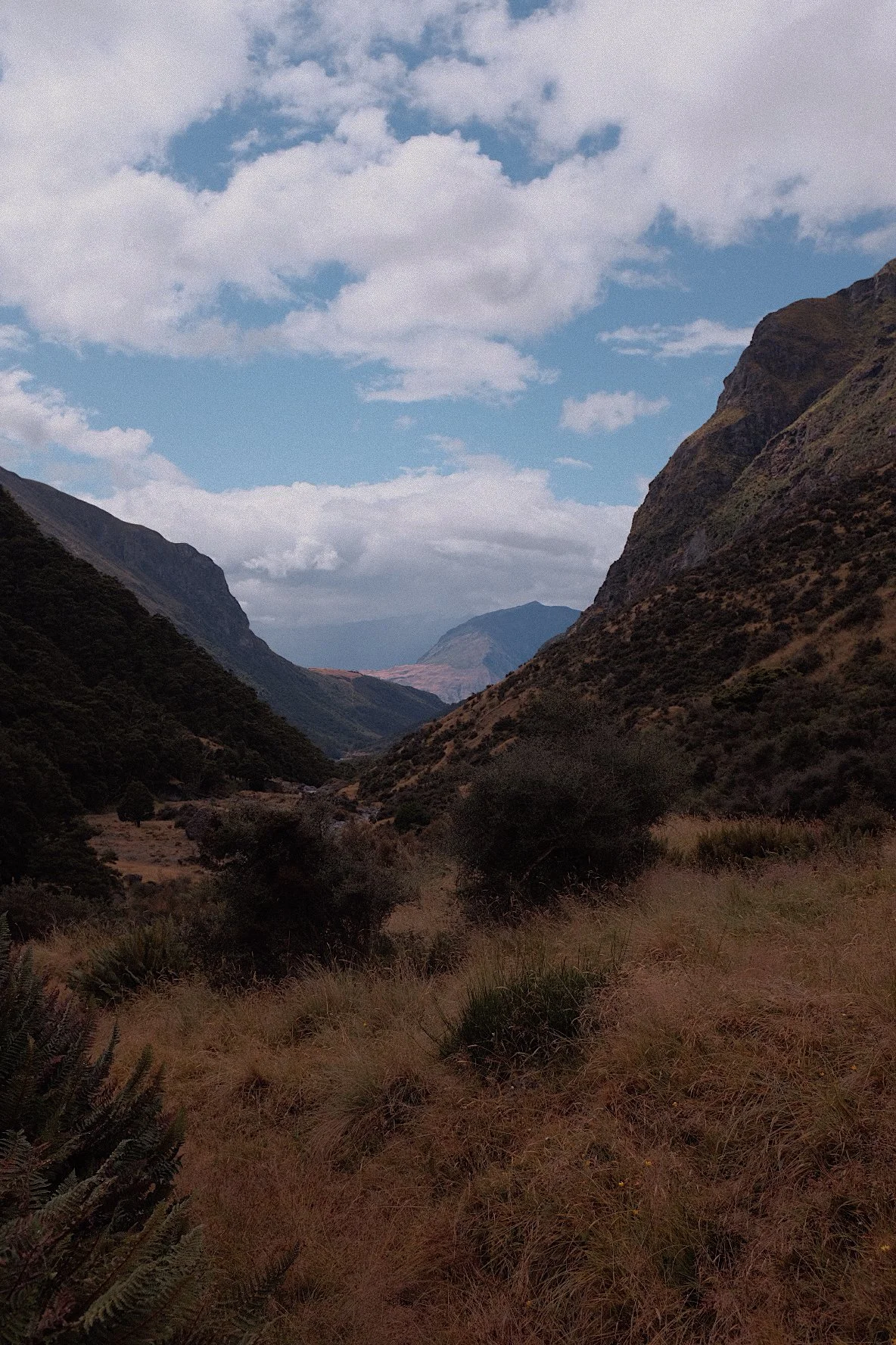 Mountain valley landscape with grassy fields and rocky hills, under a partly cloudy sky.