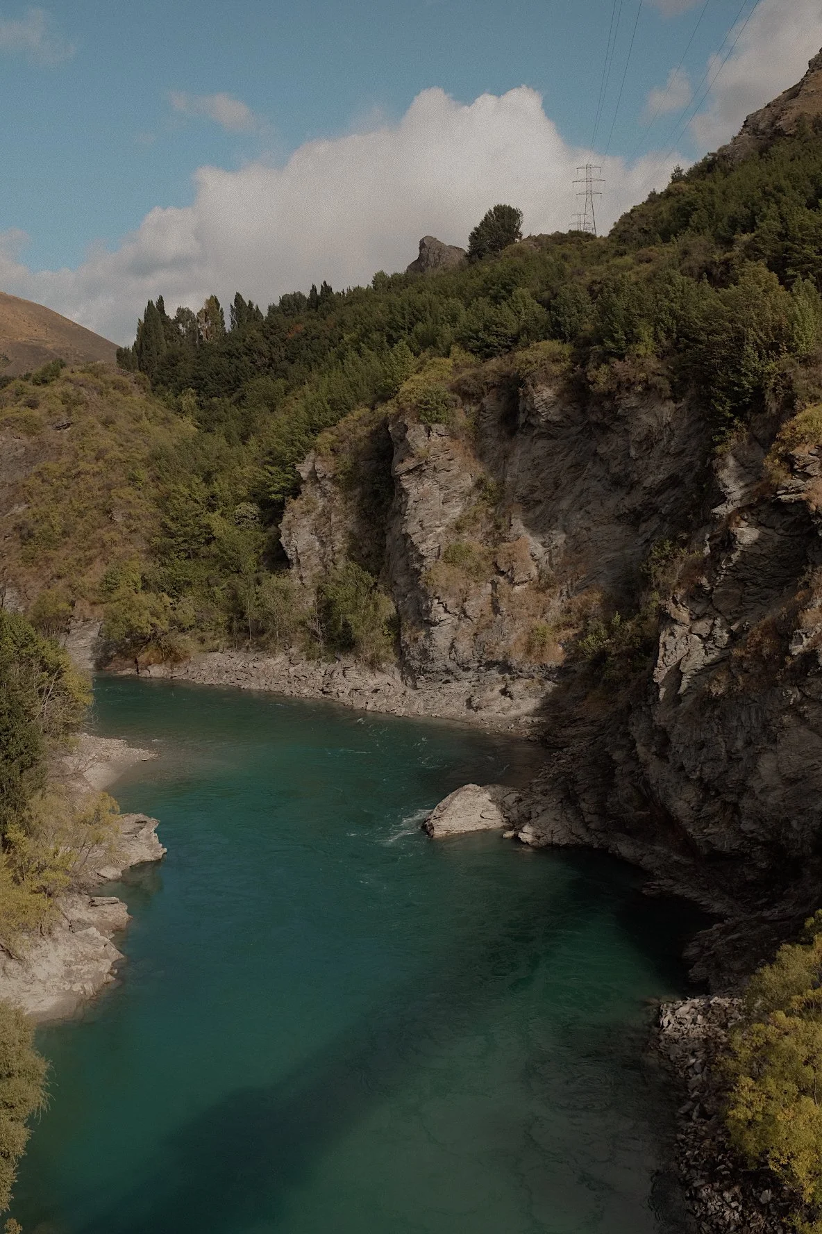 Scenic river with turquoise water flowing through rocky cliffs and lush green forest under a cloudy sky.