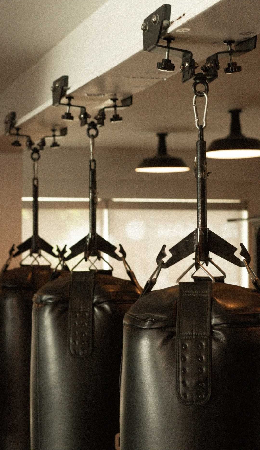 Three black punching bags hanging from a ceiling using chains and hooks in a gym or fitness studio.