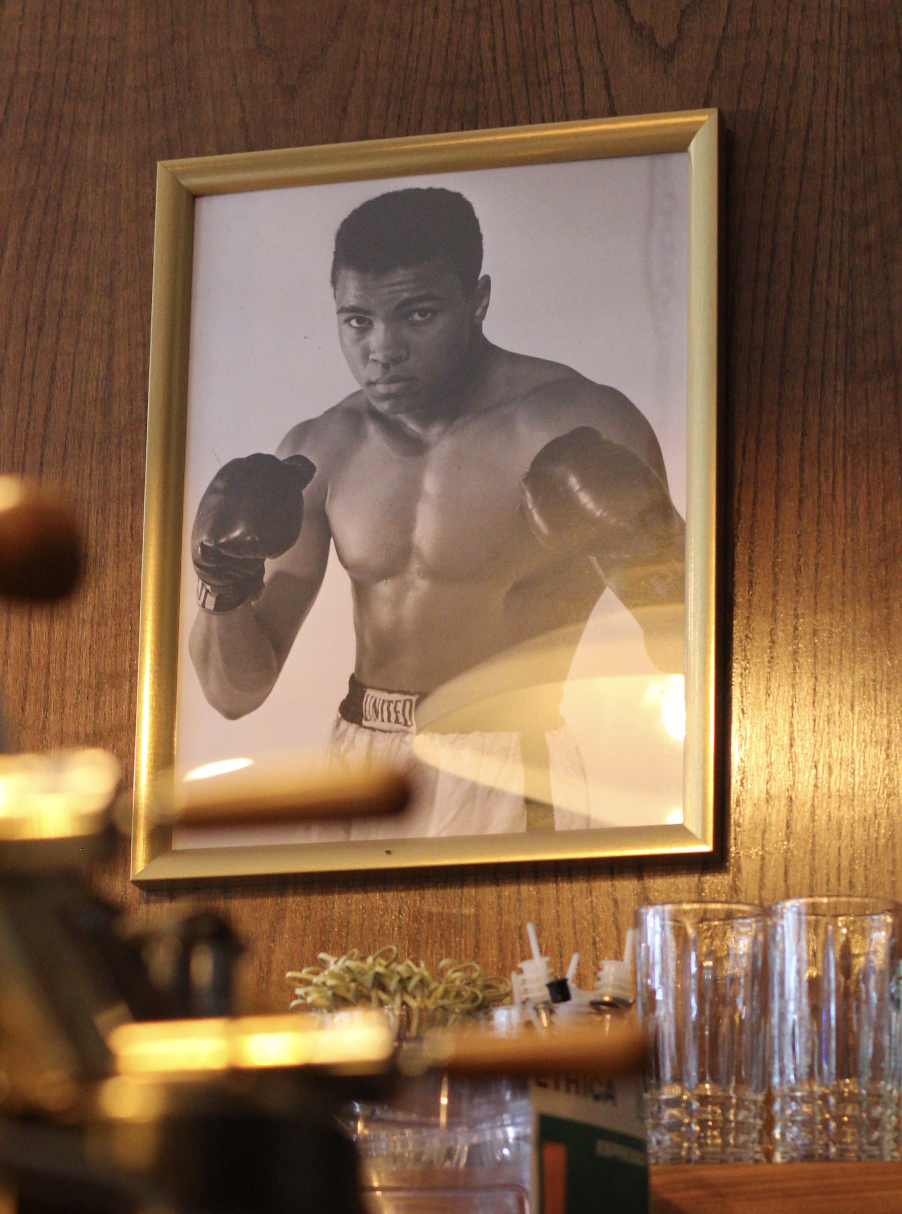 Black and white photo of a young male boxer with gloves raised in a fighting stance, framed on a wooden wall in a cafe or restaurant.