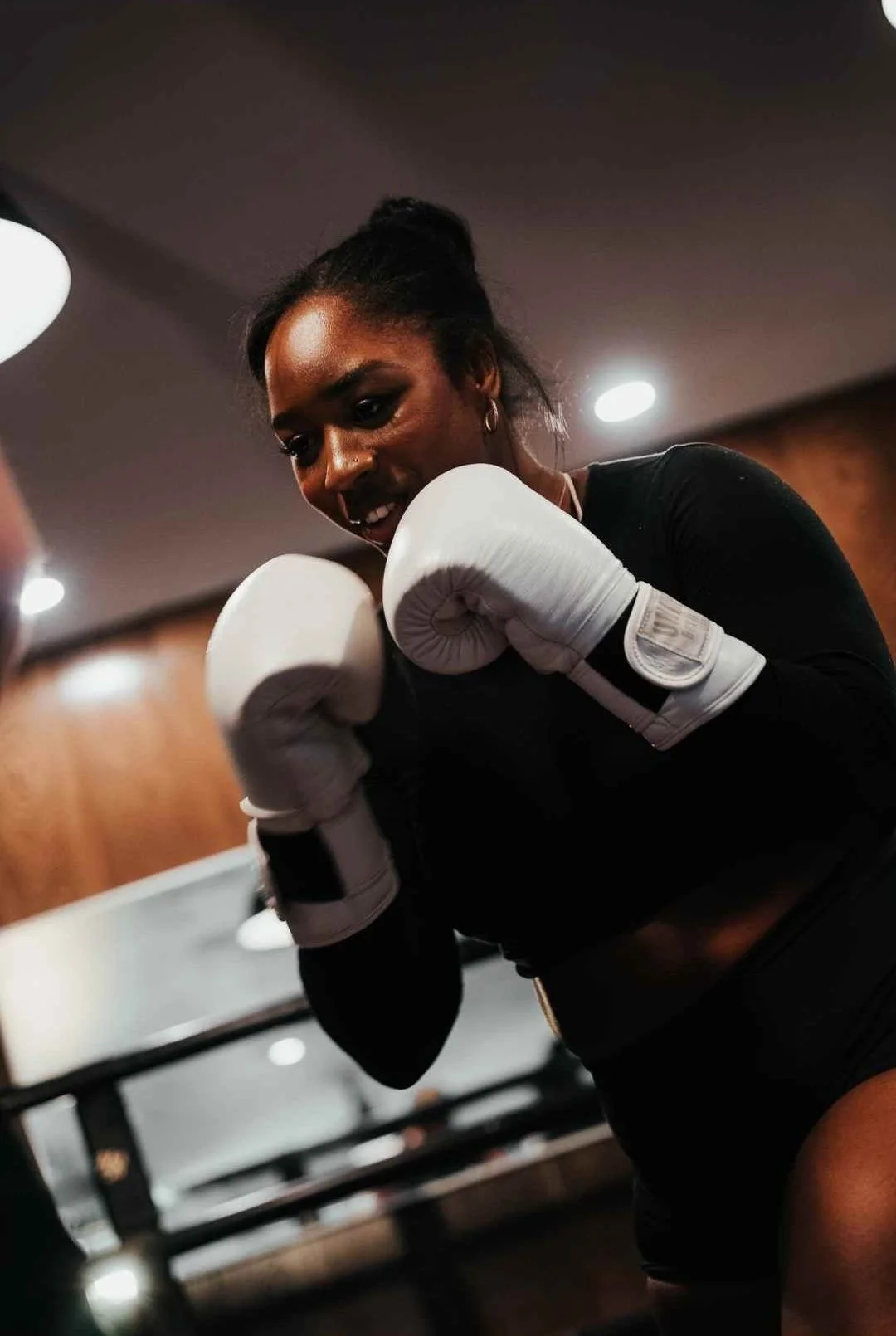 A woman wearing white boxing gloves practicing boxing in a gym.