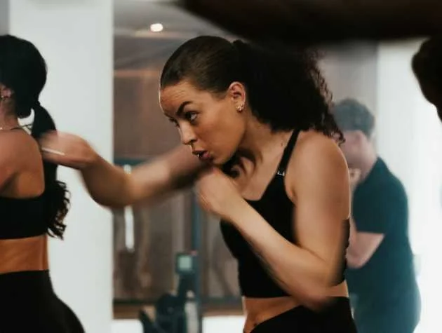 A woman practicing boxing or kickboxing in a gym, wearing athletic clothing.