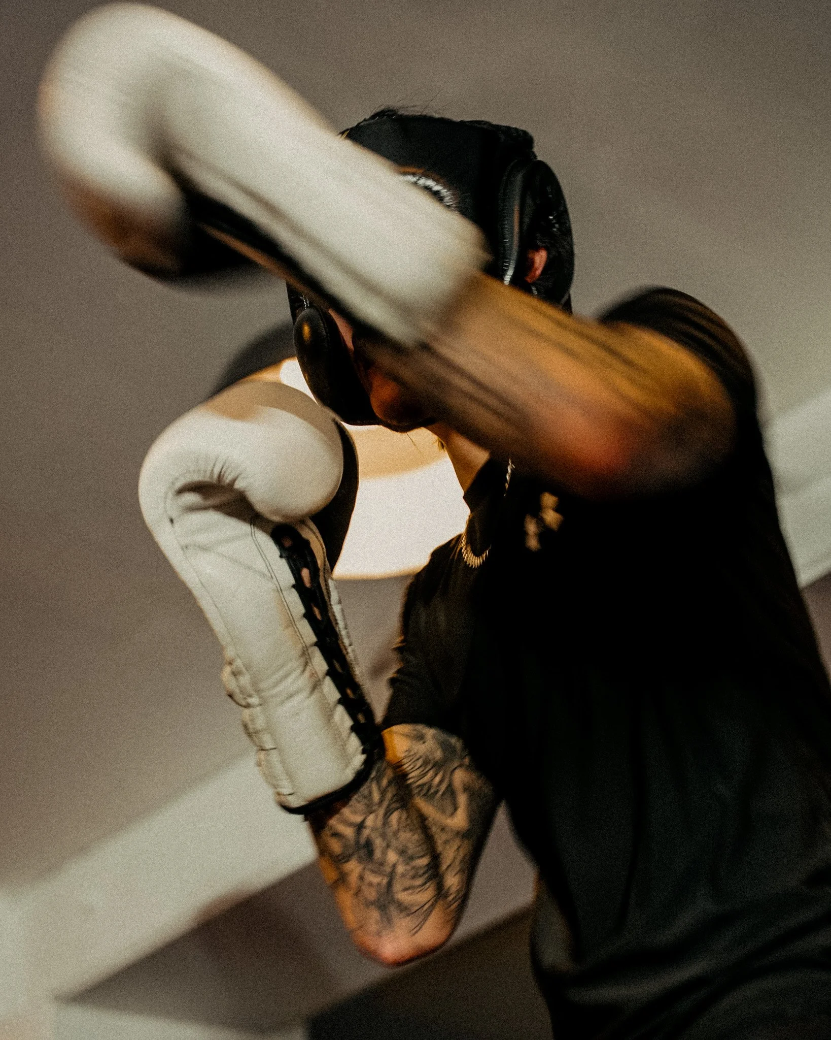 A man in a black shirt boxing with gloves on, practicing a punch. He has short light brown hair and is focused.