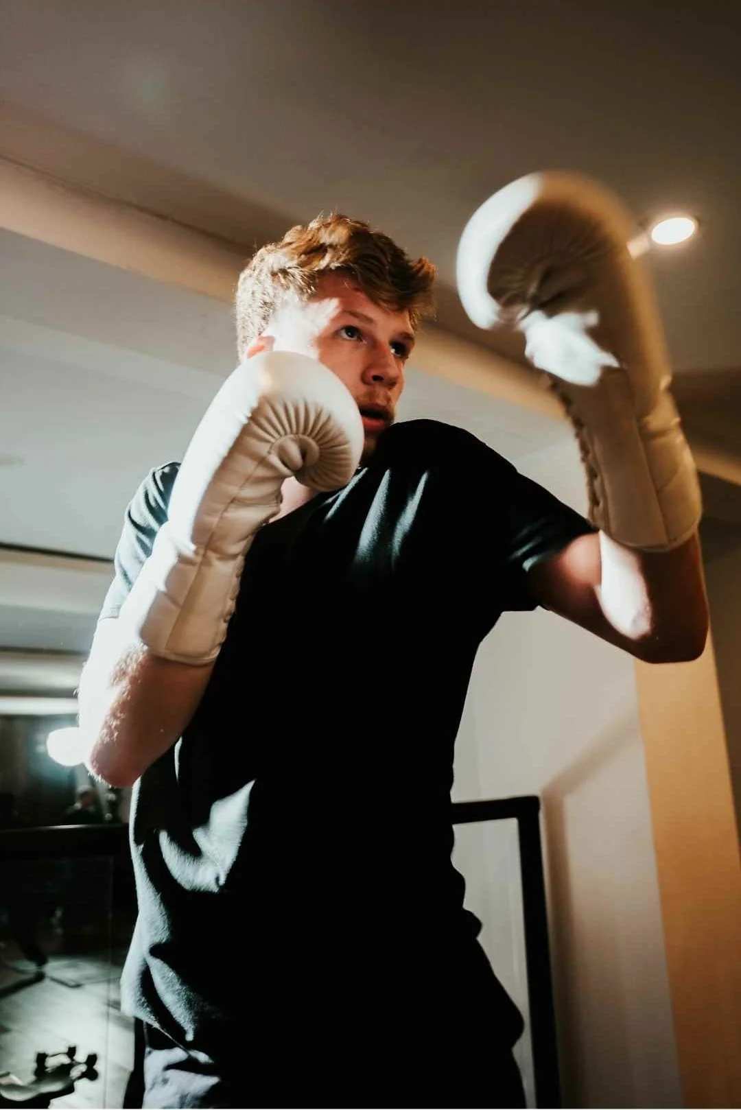 A young man wearing boxing gloves in a fighting stance indoors.