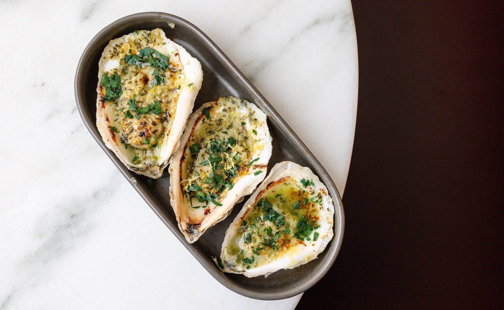 Broiled oysters at Shy Shy in Chelsea, NYC, topped with herbed butter, breadcrumbs and fresh parsley. A signature dish perfect for pairing with craft cocktails and martinis.
