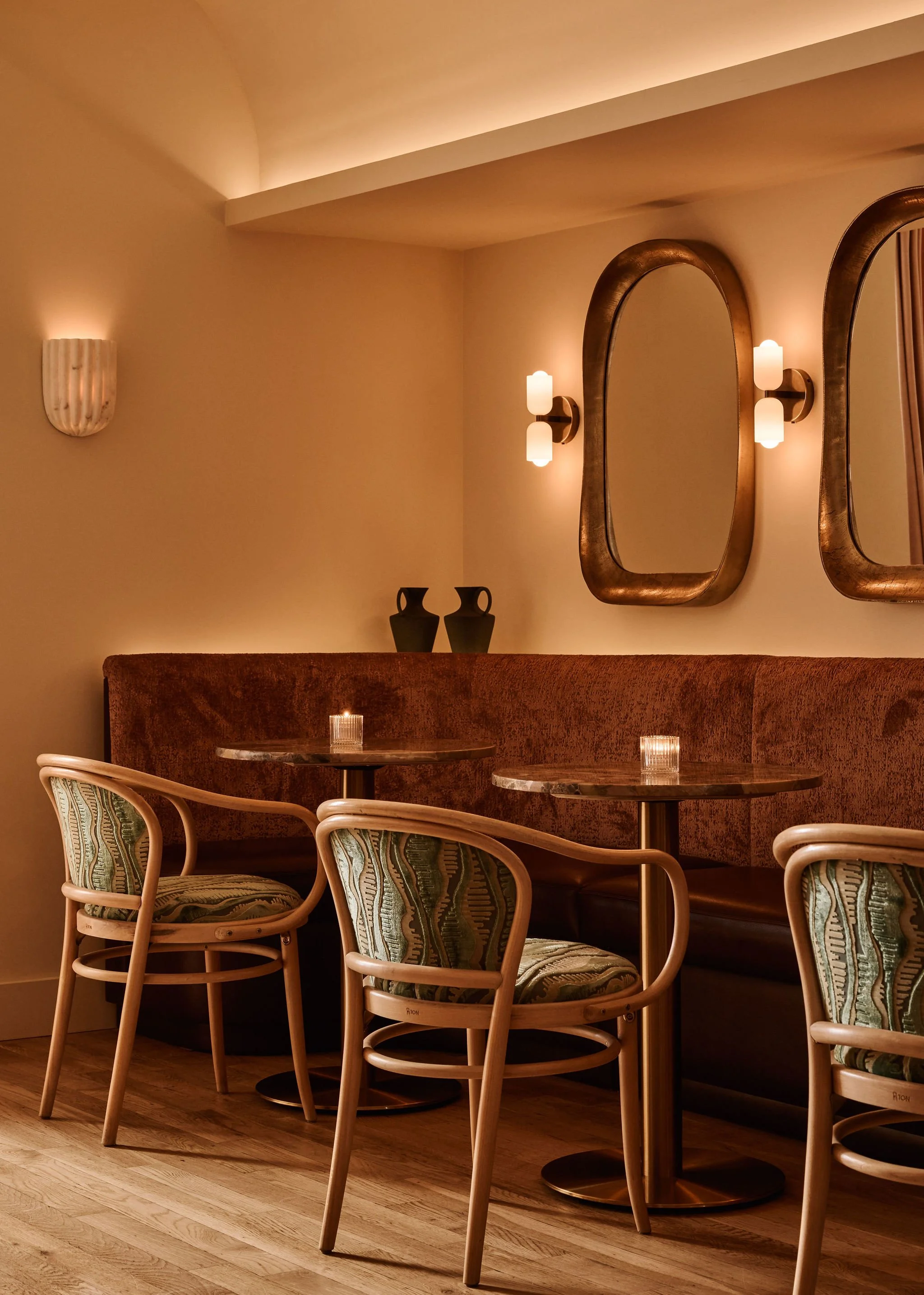 Interior of Shy Shy cocktail bar in Chelsea, featuring warm lighting, curved mirrors, velvet banquette seating, and mid-century chairs — a cozy, Pacific Northwest–inspired space for cocktails and small plates.