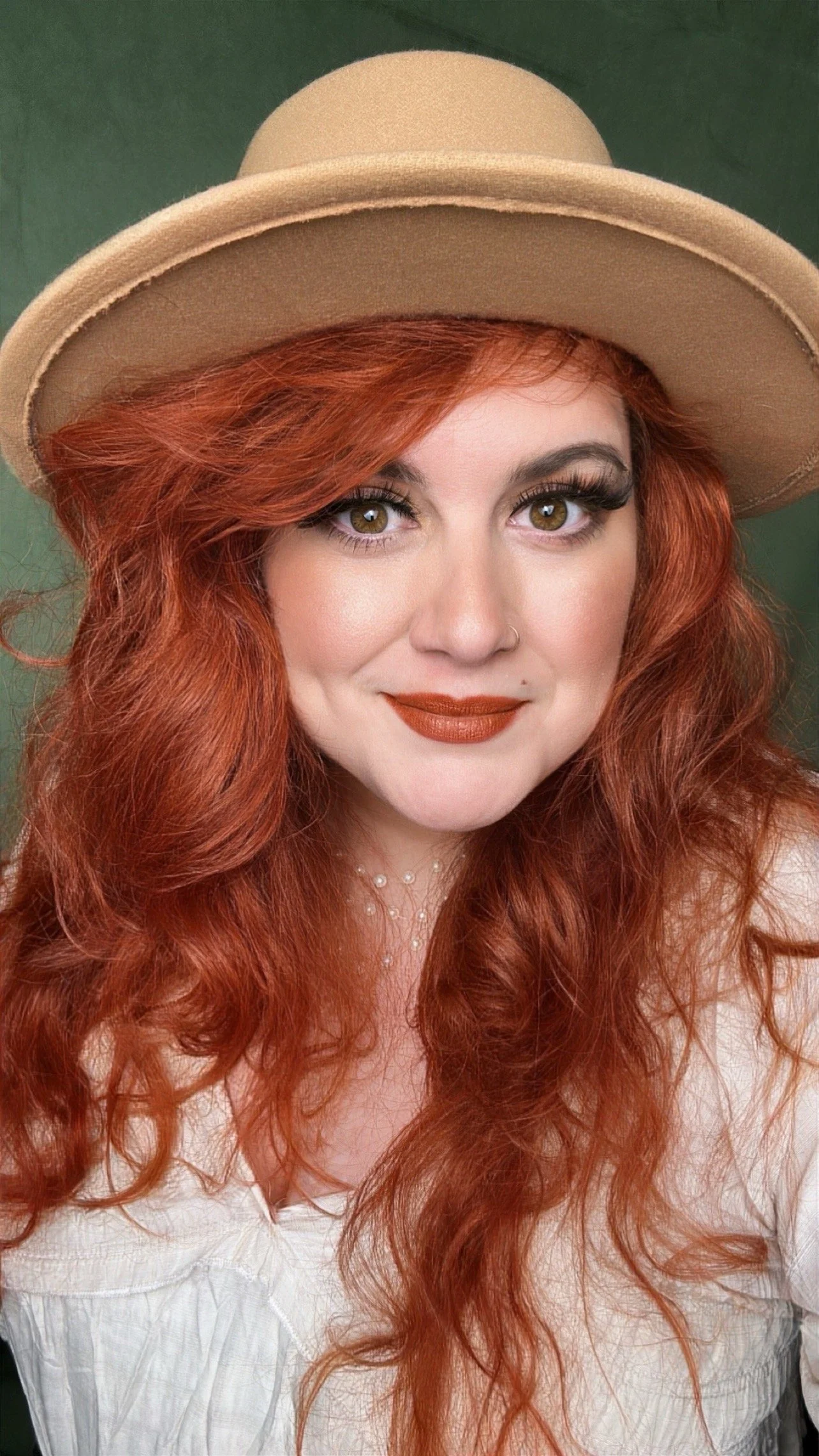 A head shot of Jennifer, she has long red hair wearing a beige hat and a white blouse, smiling.