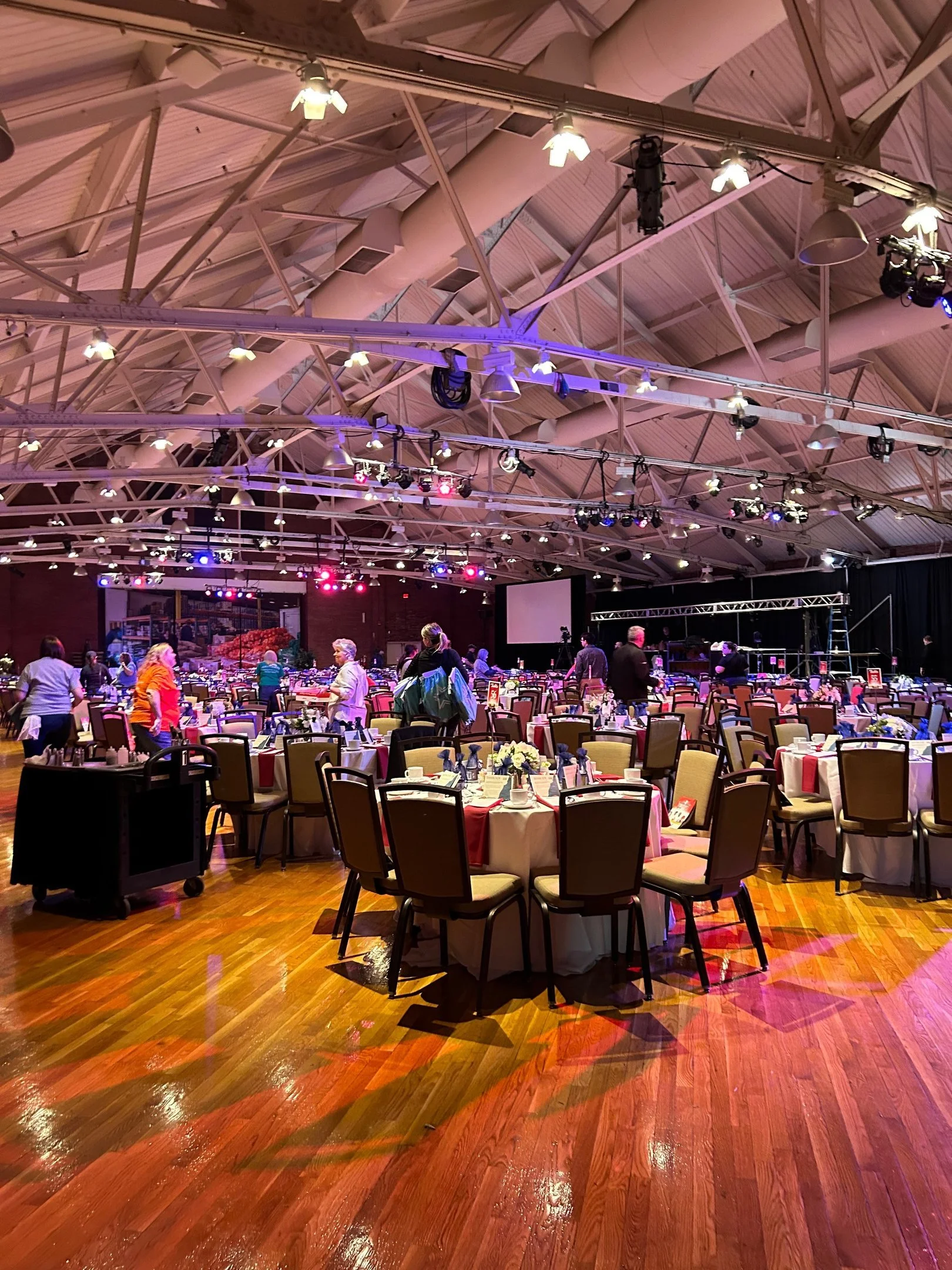 Banquet hall with round tables and chairs, colorful lighting, and people mingling.