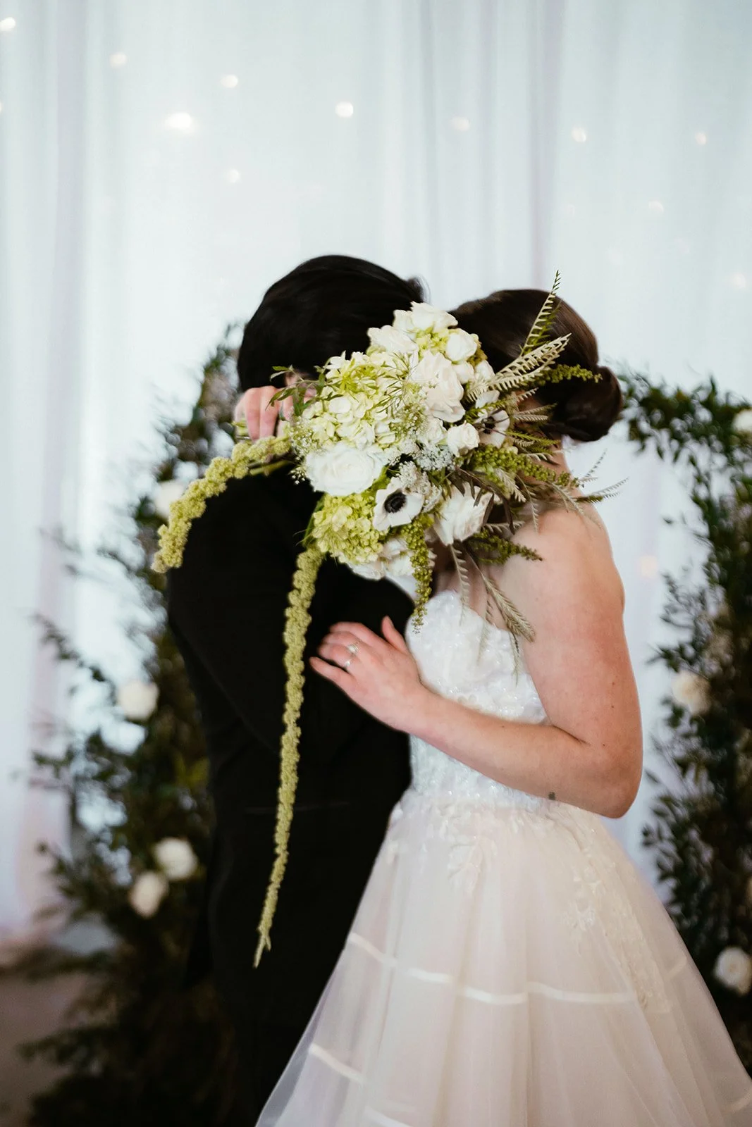 Wedding couple kissing behind bouquet, bride in white dress