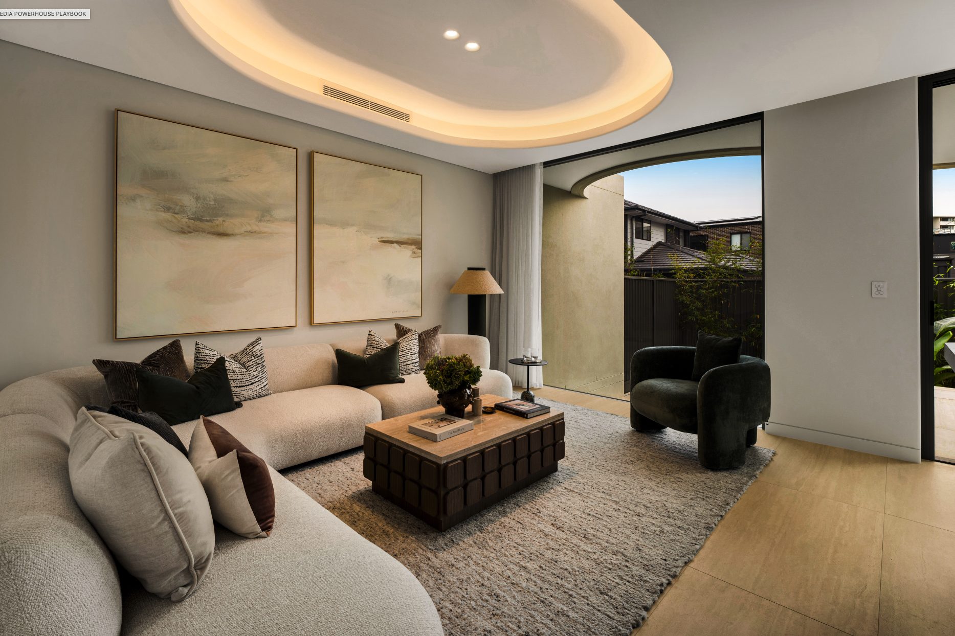 Modern living room with neutral color palette, featuring a large beige sofa with multiple black, white, and patterned pillows, a wooden coffee table with books and a plant, a black armchair, and wall art with abstract paintings. Large sliding glass d