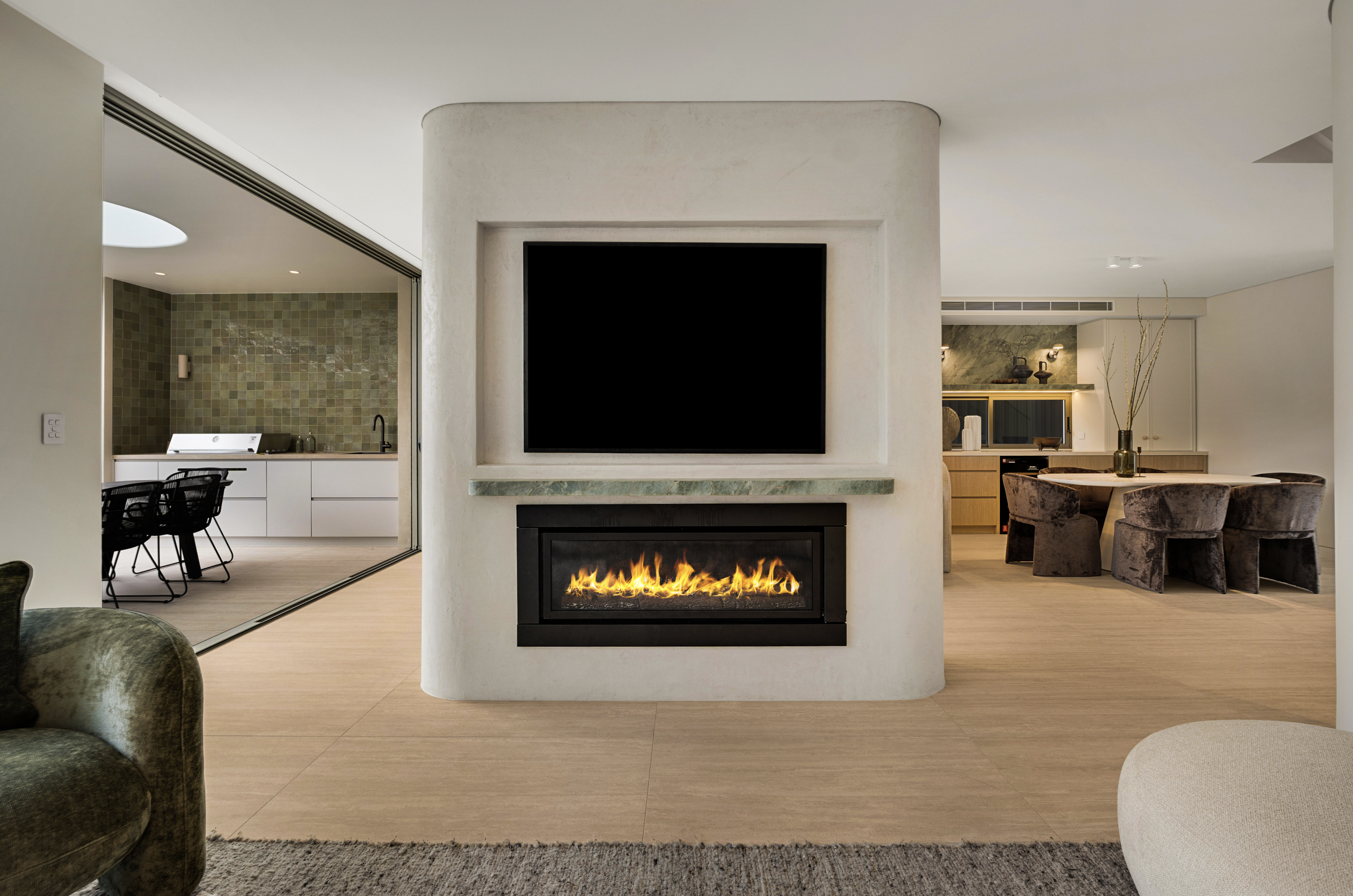 Modern living room with a fireplace, flat-screen TV, dining area, and open kitchen in the background.