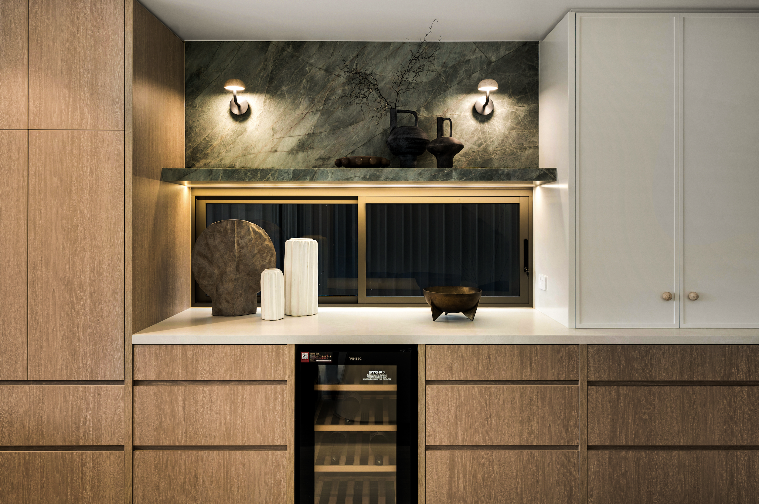 Modern kitchen cabinet with a green marble backsplash, decorative vases, and ambient lighting.