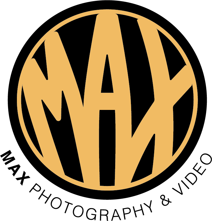 A circular logo with the word "MAYDAY" stylized inside in bold orange letters on a black background.