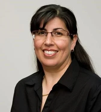 A woman with dark hair, wearing glasses and a black shirt, smiling at the camera.
