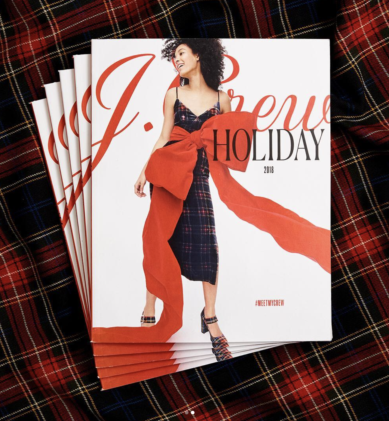 J.Crew holiday catalog cover featuring a woman in a plaid dress with a large red bow, on top of a red plaid background.