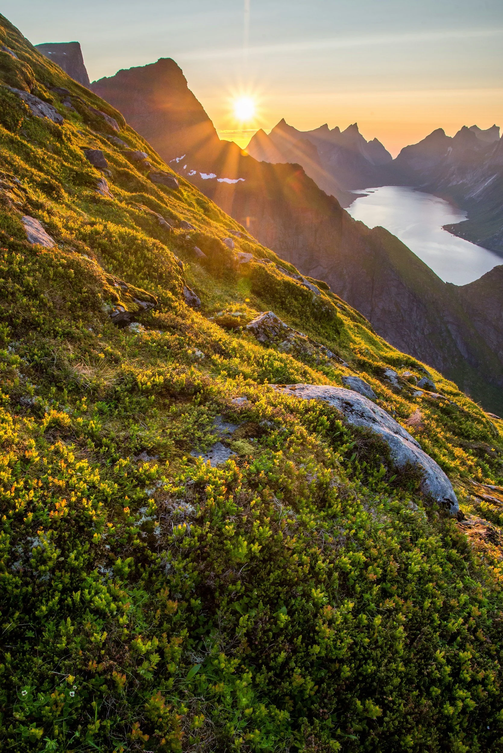 Sunset over mountain range with lush green vegetation in the foreground and a river flowing through the valley.