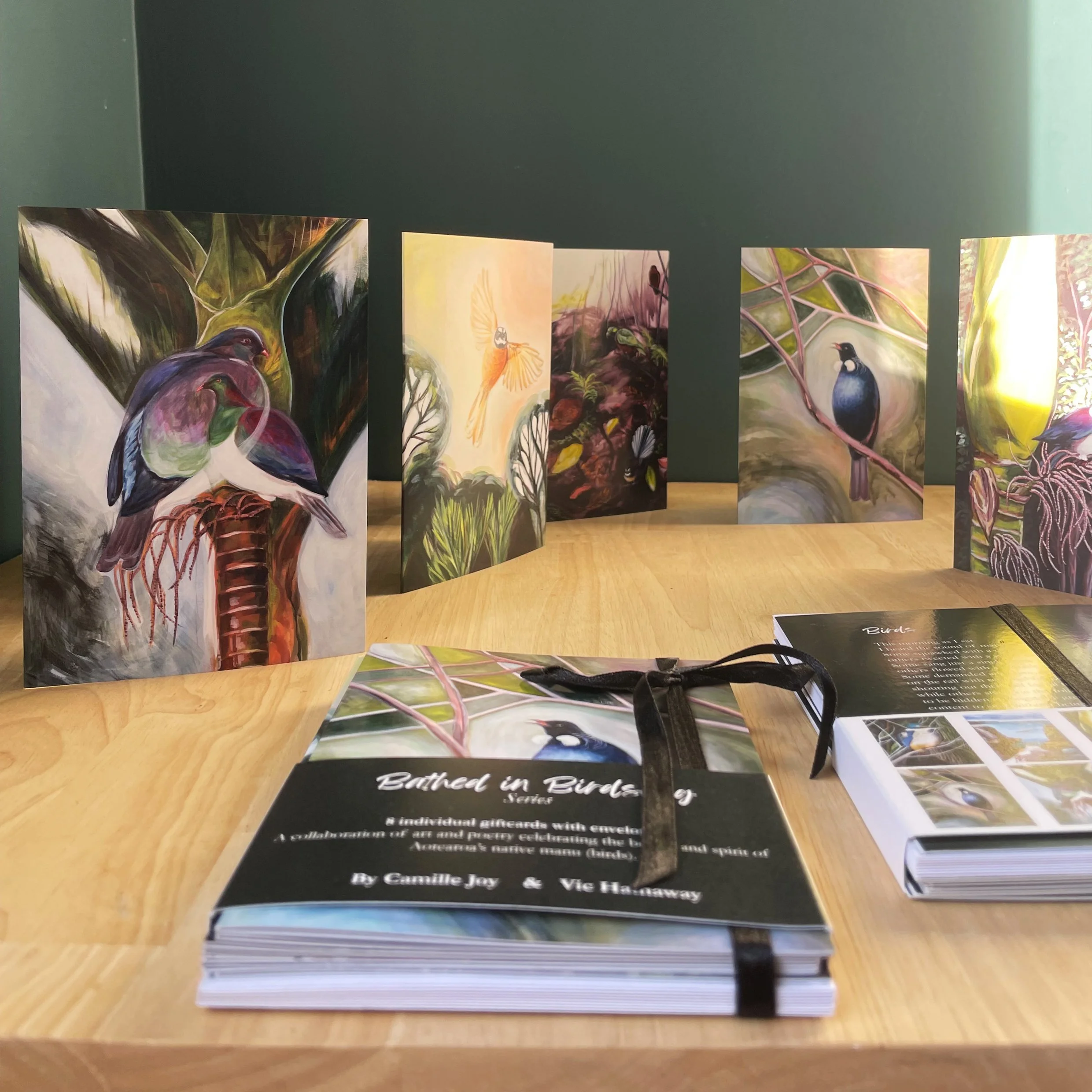 Display of illustrated cards featuring hummingbirds on a wooden table, with a booklet titled 'Batched in Bird' beside it.