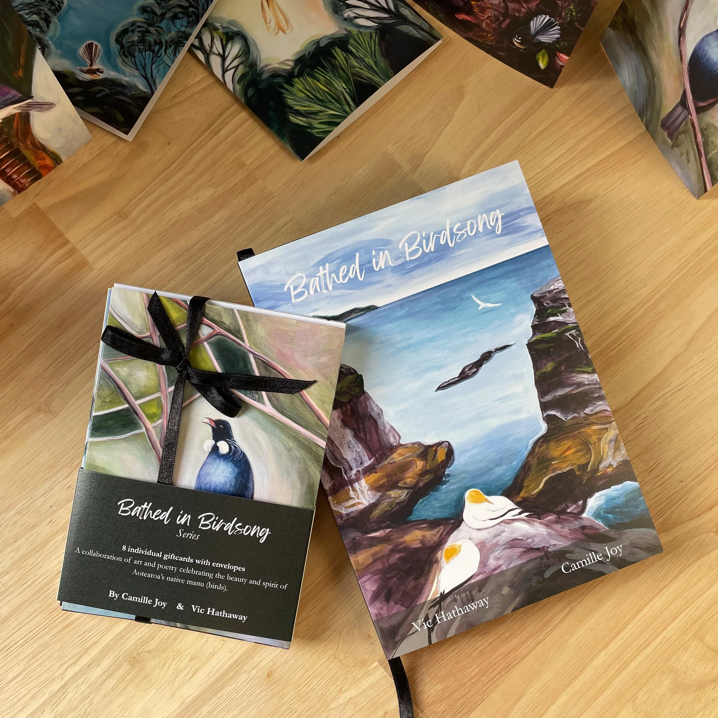 Books titled 'Batched in Birdsong' featuring bird illustrations and a landscape scene with rocks and the ocean.