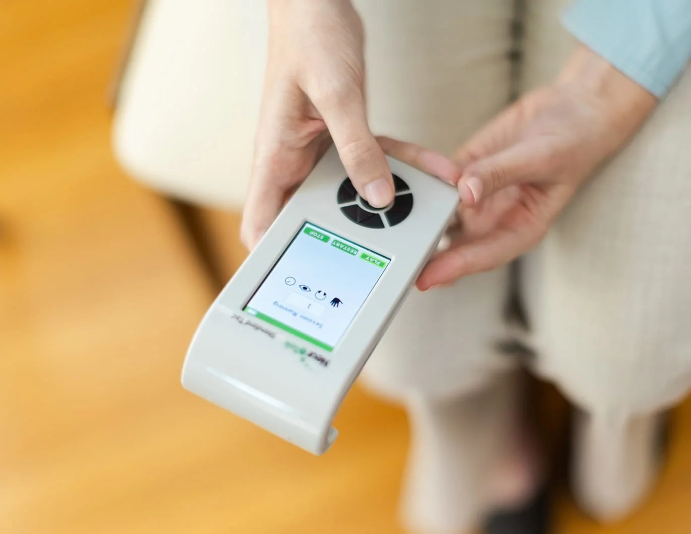 Michele Root, LCSW holds and operates an EMDR handheld device with a display screen and control buttons, viewed from above against a neutral background.