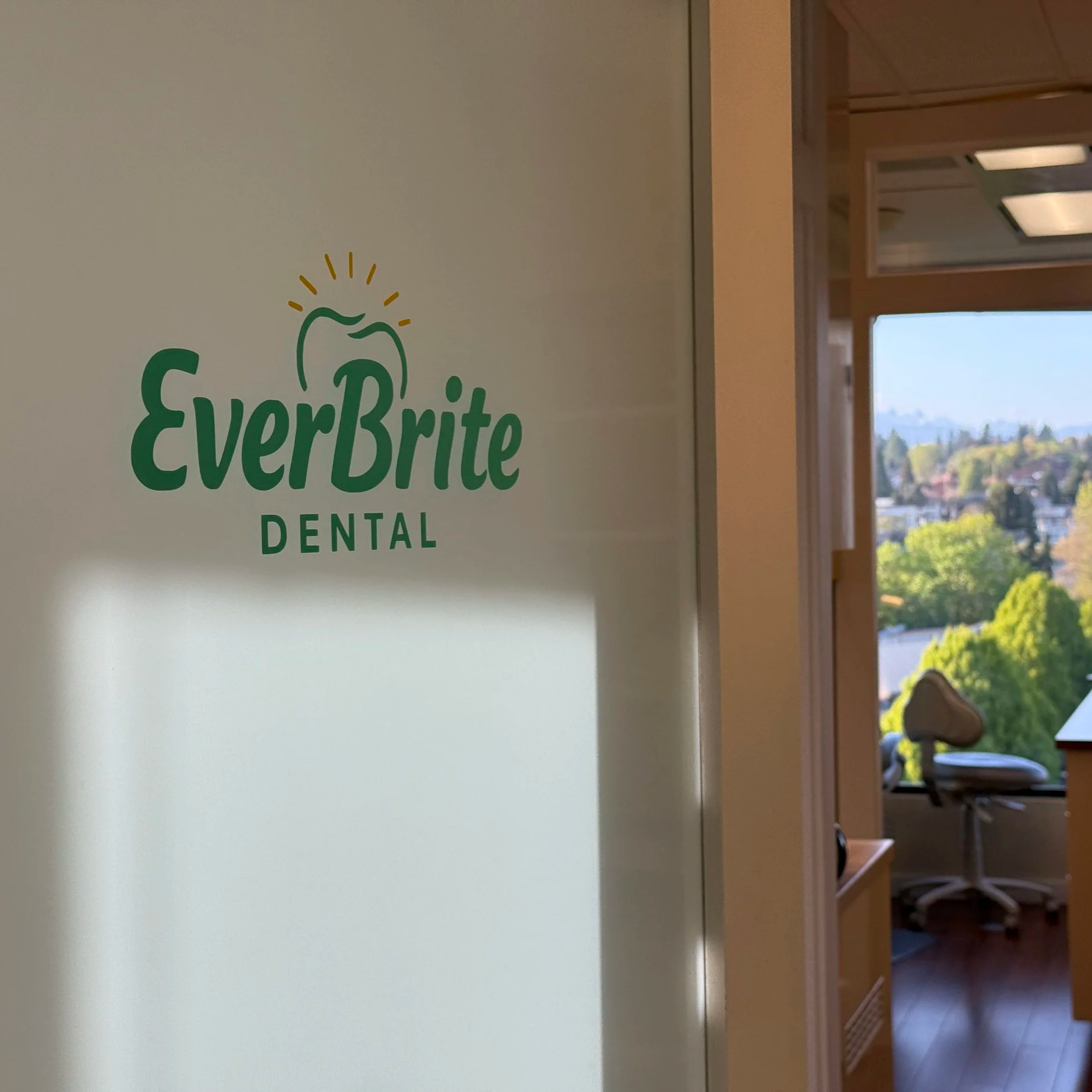 Glass door with "EverBrite Dental" logo and view of dental office interior with examination chair and windows overlooking greenery.