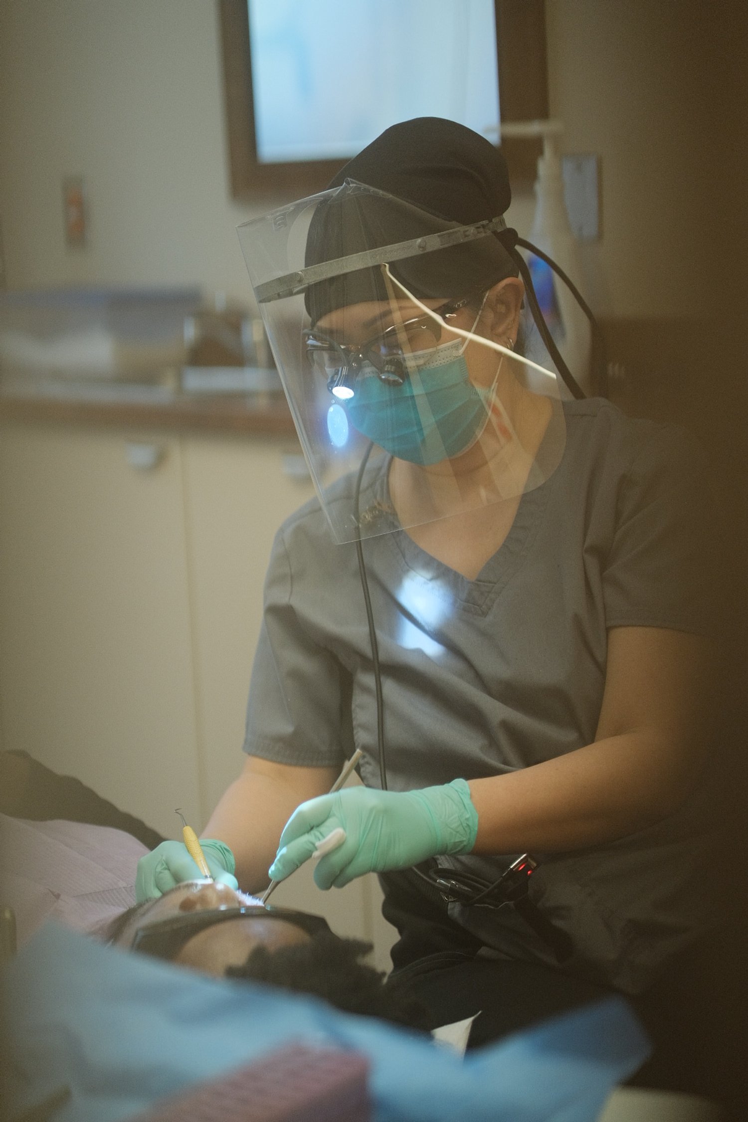 Dental professional wearing scrubs and face shield performing dental procedure on patient