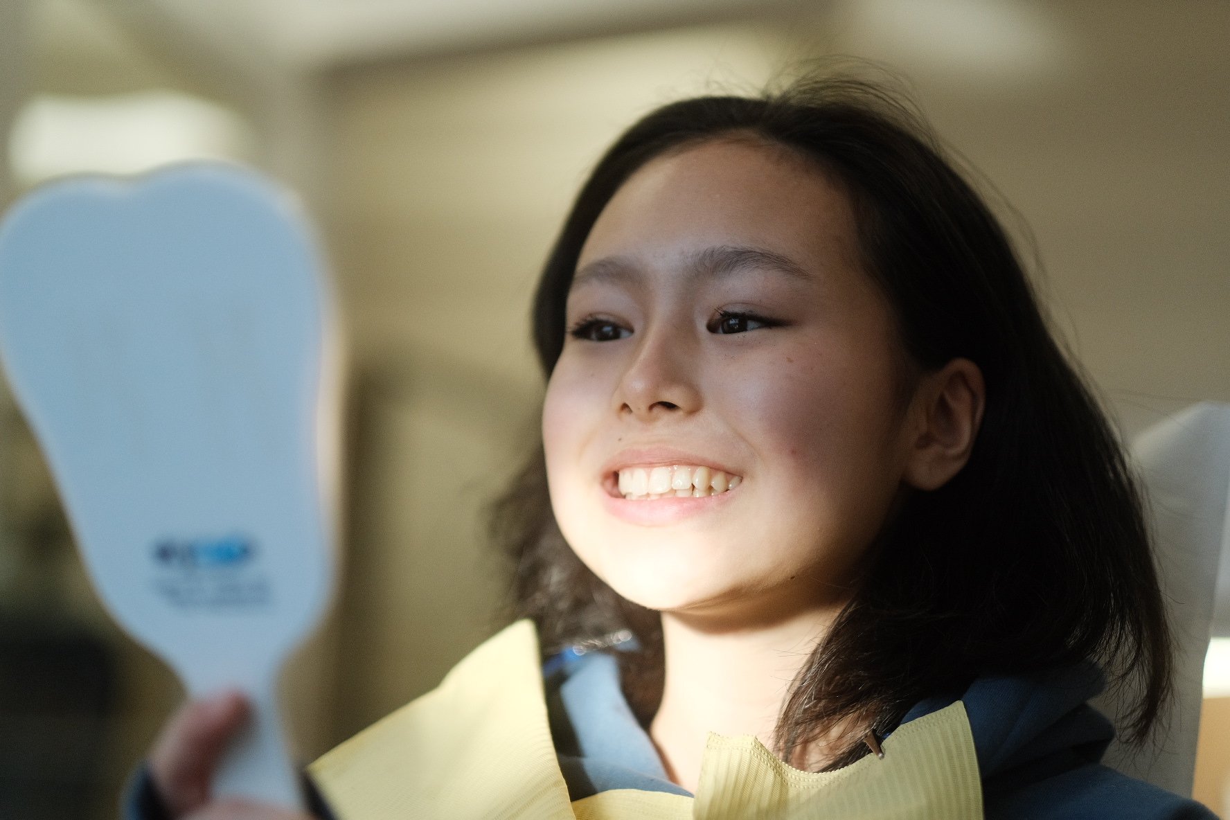 Girl looking at a handheld dentist mirror, smiling, indoors.