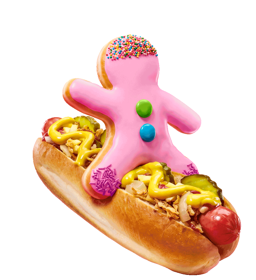 Hot dog topped with colorful sprinkles, chopsticks, and a gingerbread man cookie decorated with pink icing and M&M candies, placed on a hot dog bun with mustard, relish, and onions.