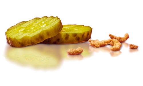 A sliced pickle with a few loose pieces beside it on a reflective surface.