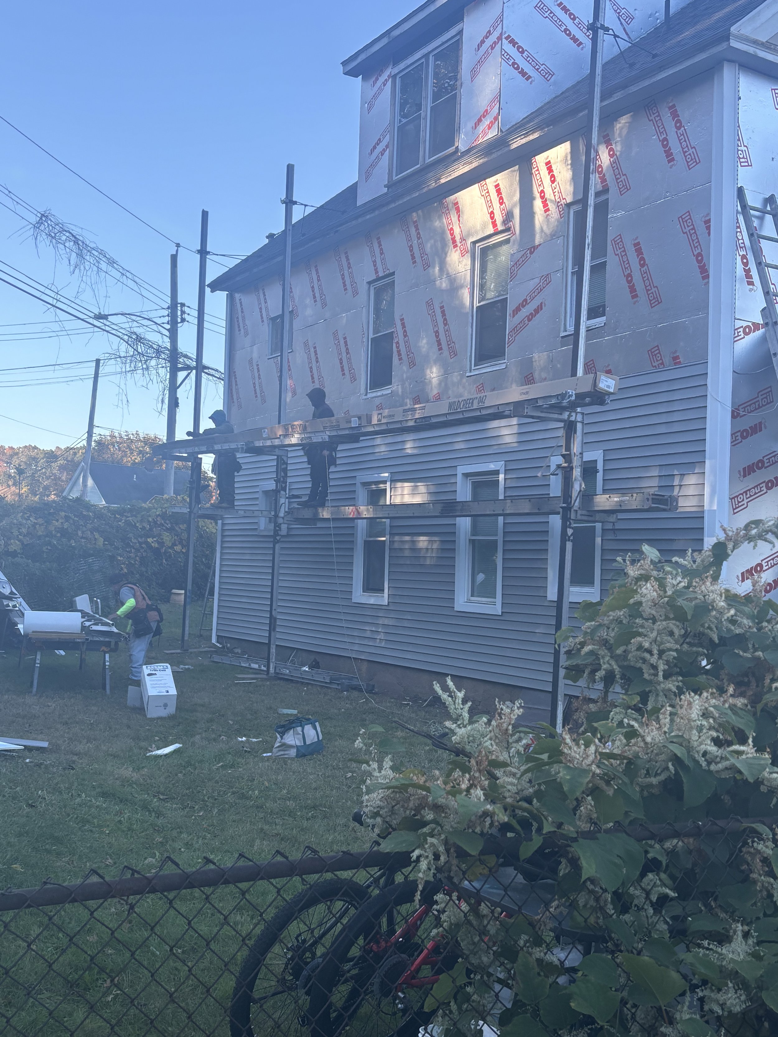 Construction workers on scaffolding working on the exterior of a residential house that is under renovation or construction, with building materials and tools around.