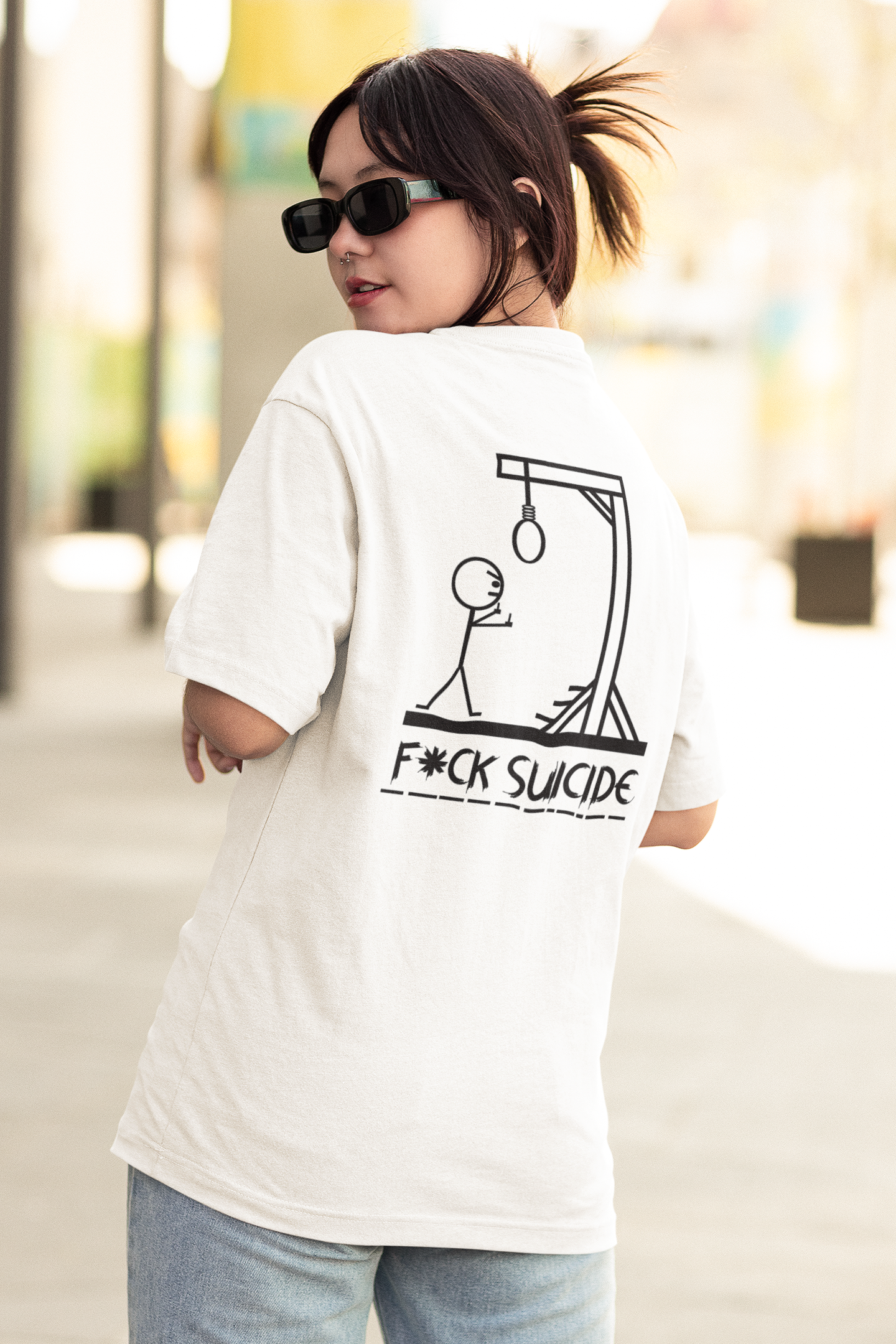 A young woman with dark hair and sunglasses, looking over her shoulder, wearing a white T-shirt with a graphic and text that says 'F*ck Suicide.'