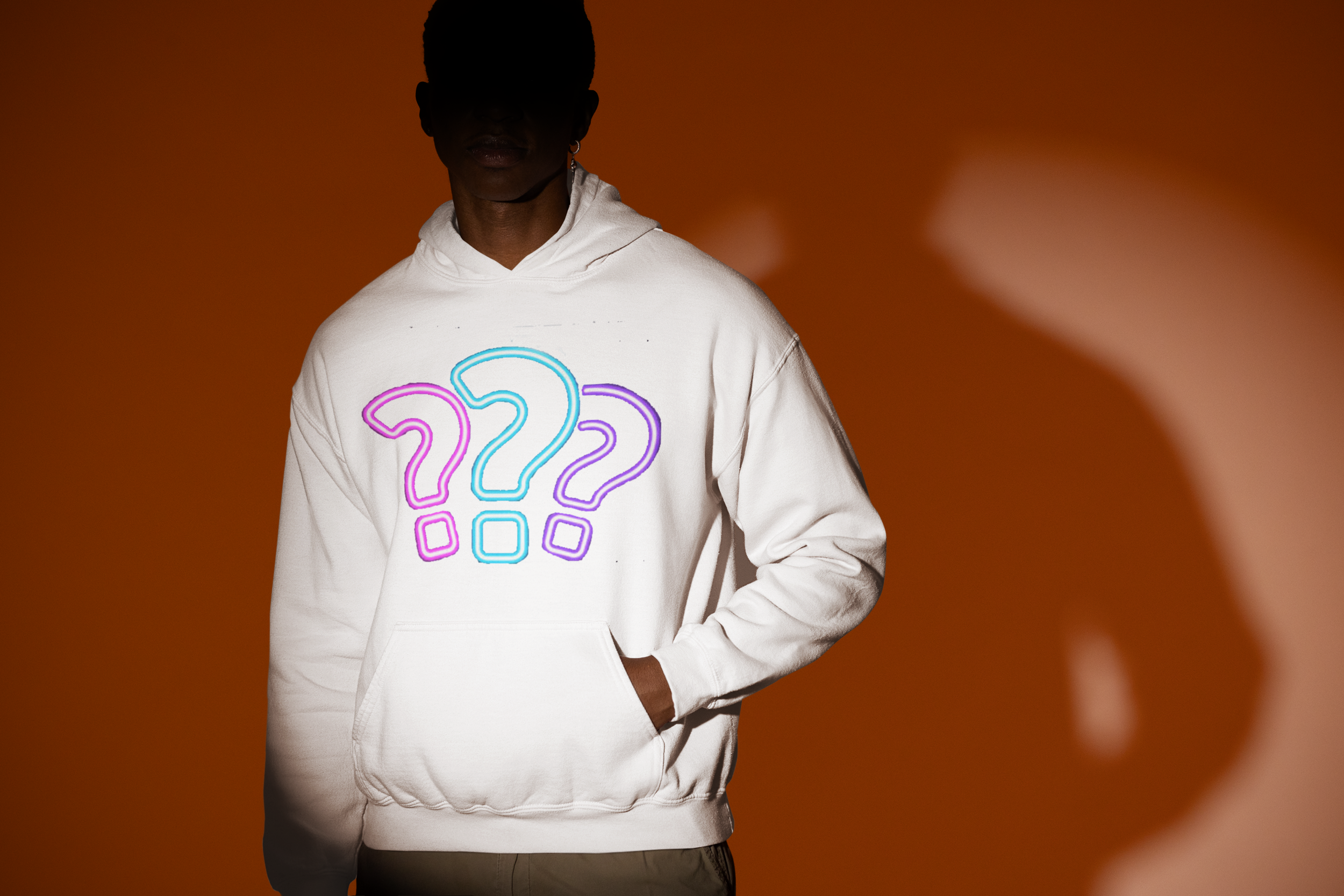 Person wearing a white hoodie with colored question marks on the front, standing against an orange background with a large shadow.