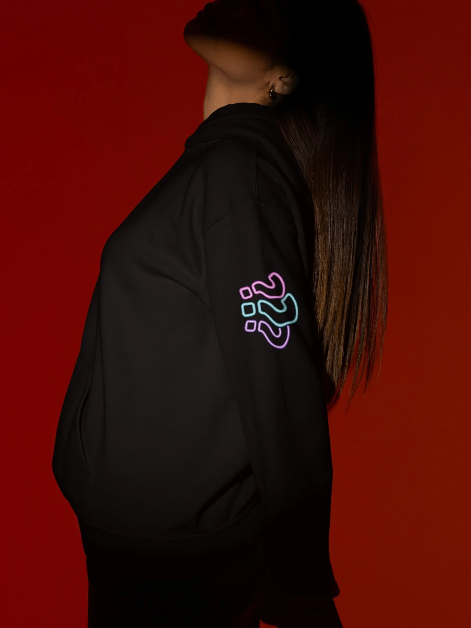 Side view of a woman with long brown hair wearing a black jacket with a colorful neon design on the sleeve, against a red background.