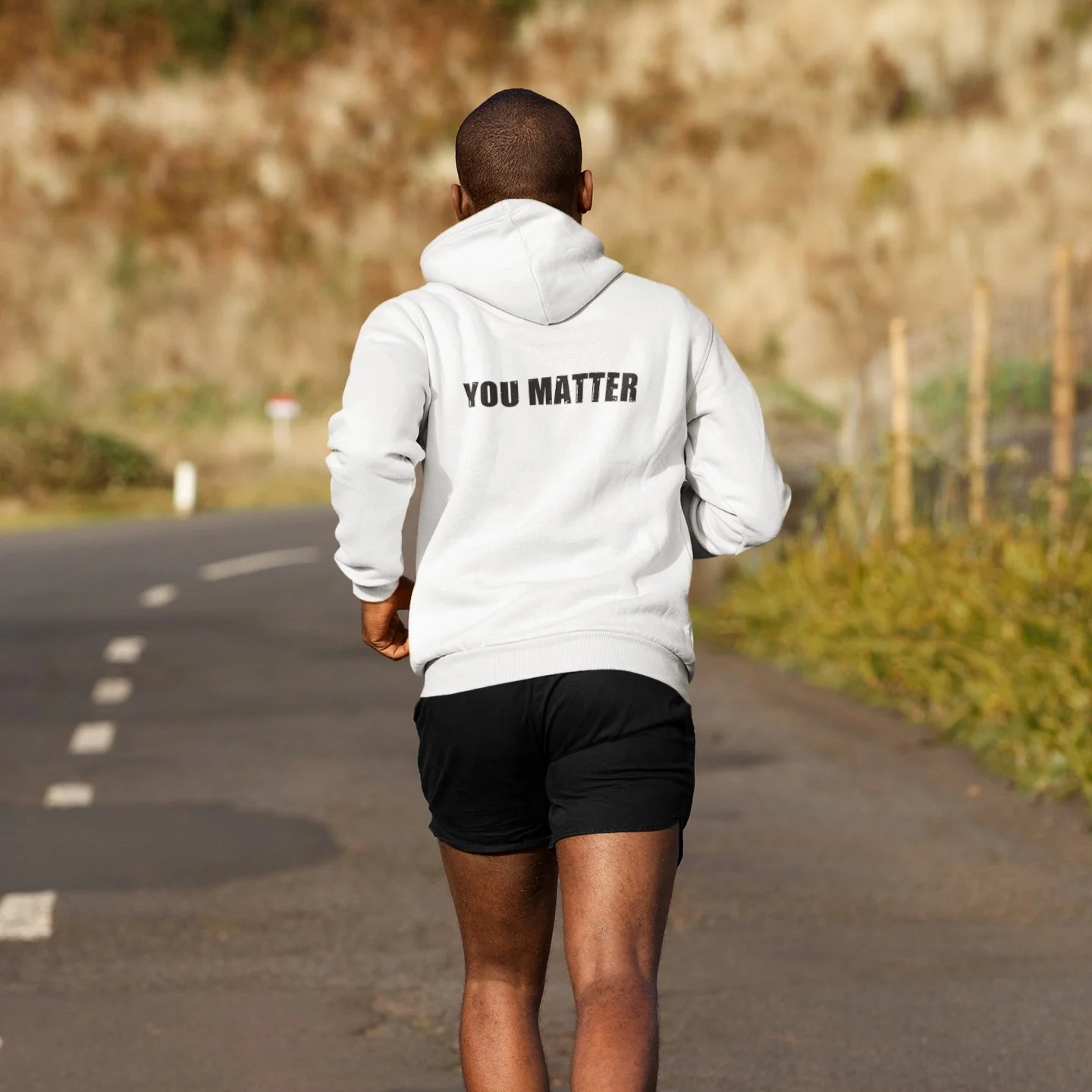 A person jogging on a road wearing a white hoodie with the words 'You Matter' on the back and black shorts.