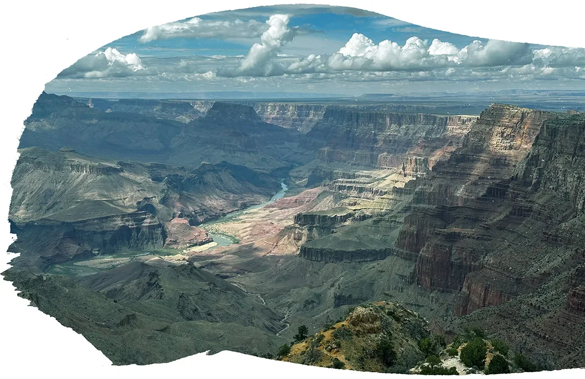 A view of the Grand Canyon with layered rock formations, a winding river at the bottom, and a partly cloudy sky overhead.