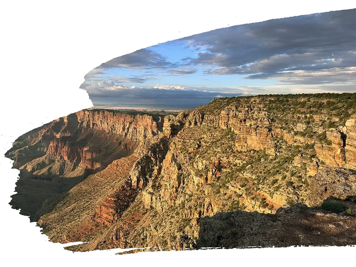 Sunset view of the Grand Canyon with layered rock formations, cliffs, and a partly cloudy sky.