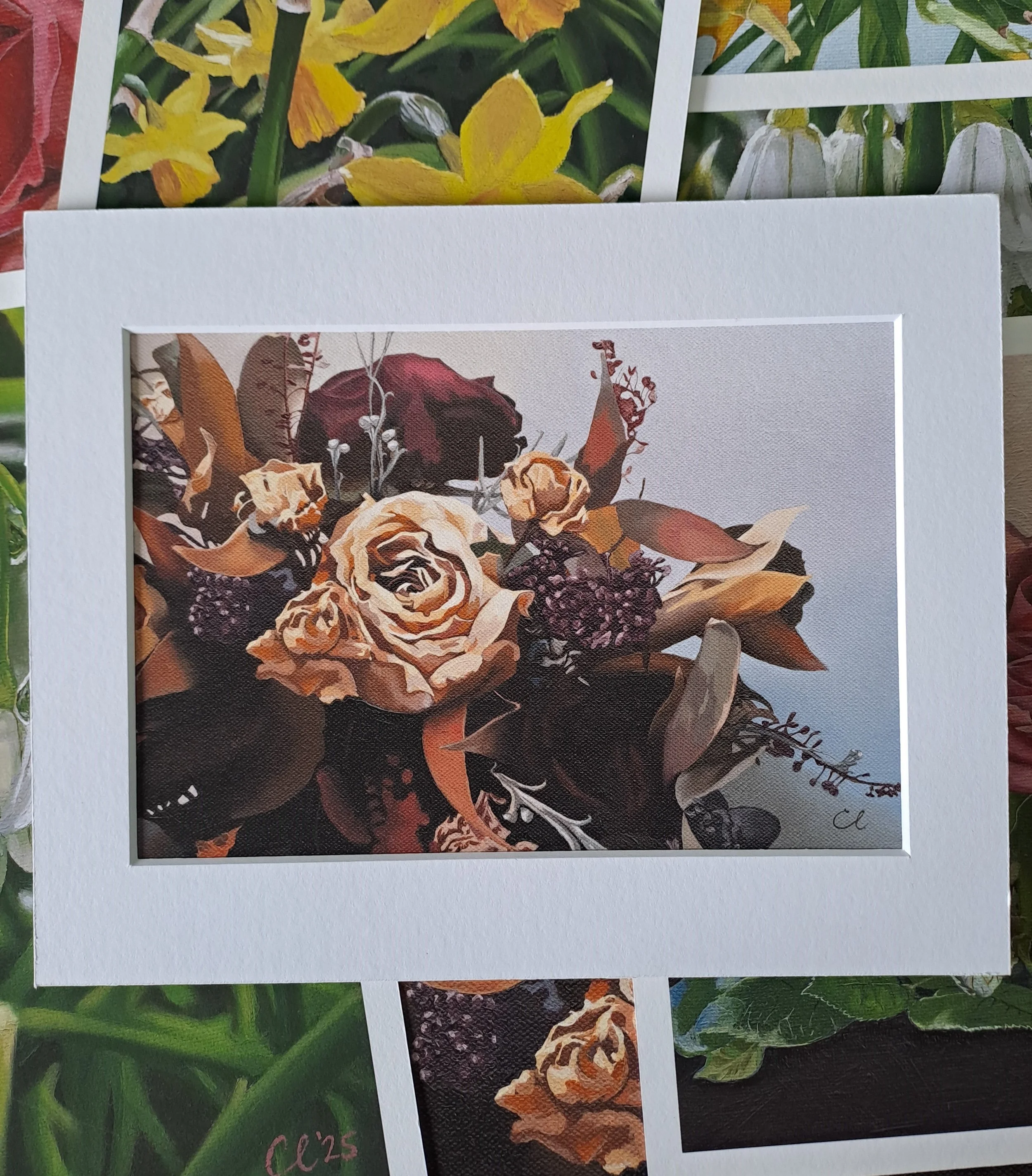 A framed picture of a floral arrangement with roses and other flowers in shades of beige, purple, and red.