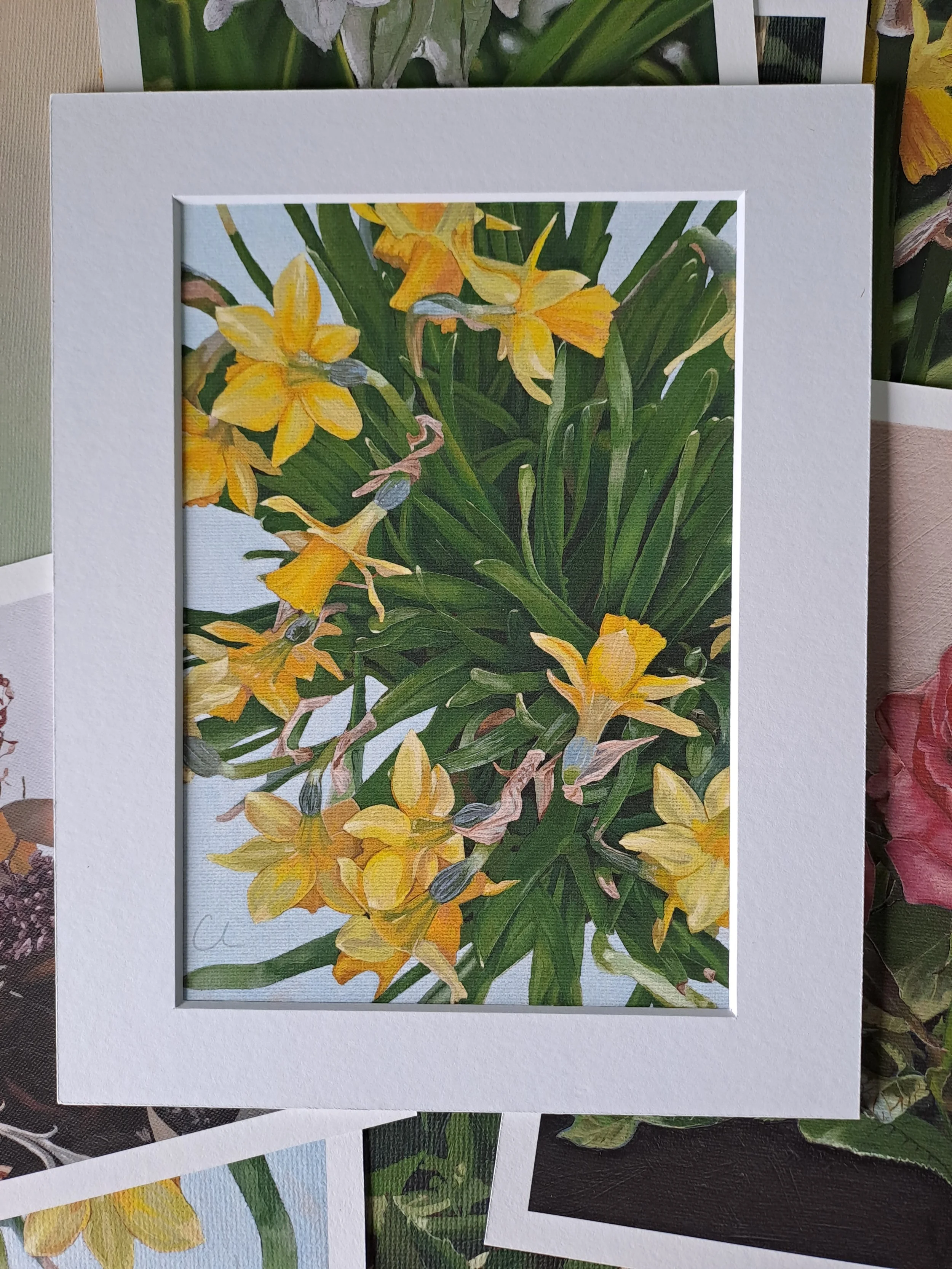 A framed picture of yellow flowers with green leaves on a white background.