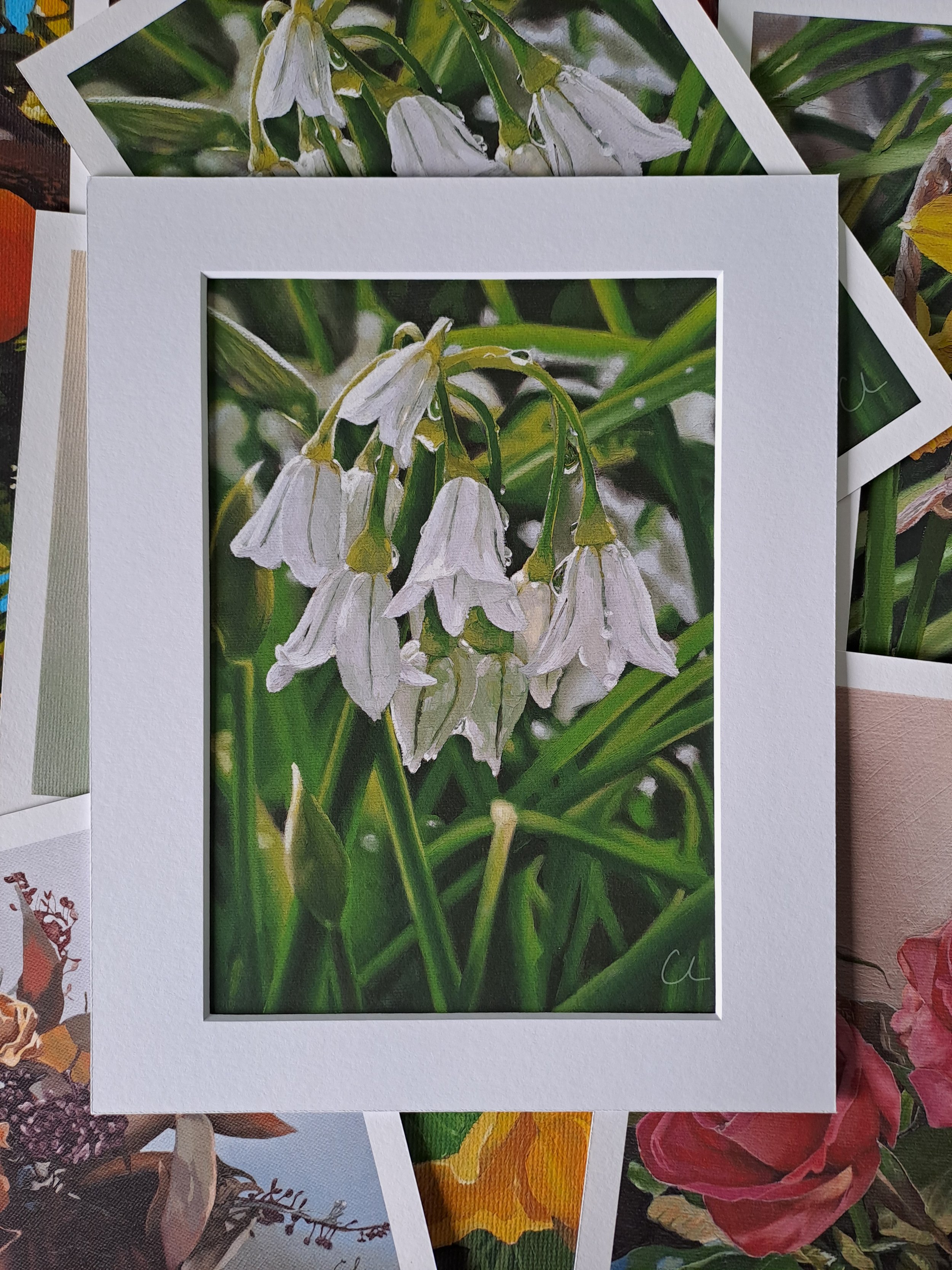 Close-up of a greeting card with an illustration of white snowdrop flowers with green stems and leaves, surrounded by other botanical illustrations.