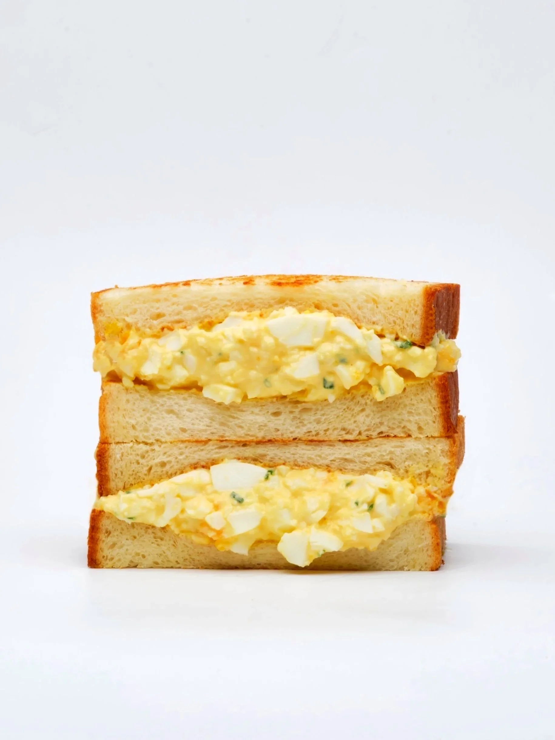 Two slices of bread with egg salad in between, stacked vertically against a white background.