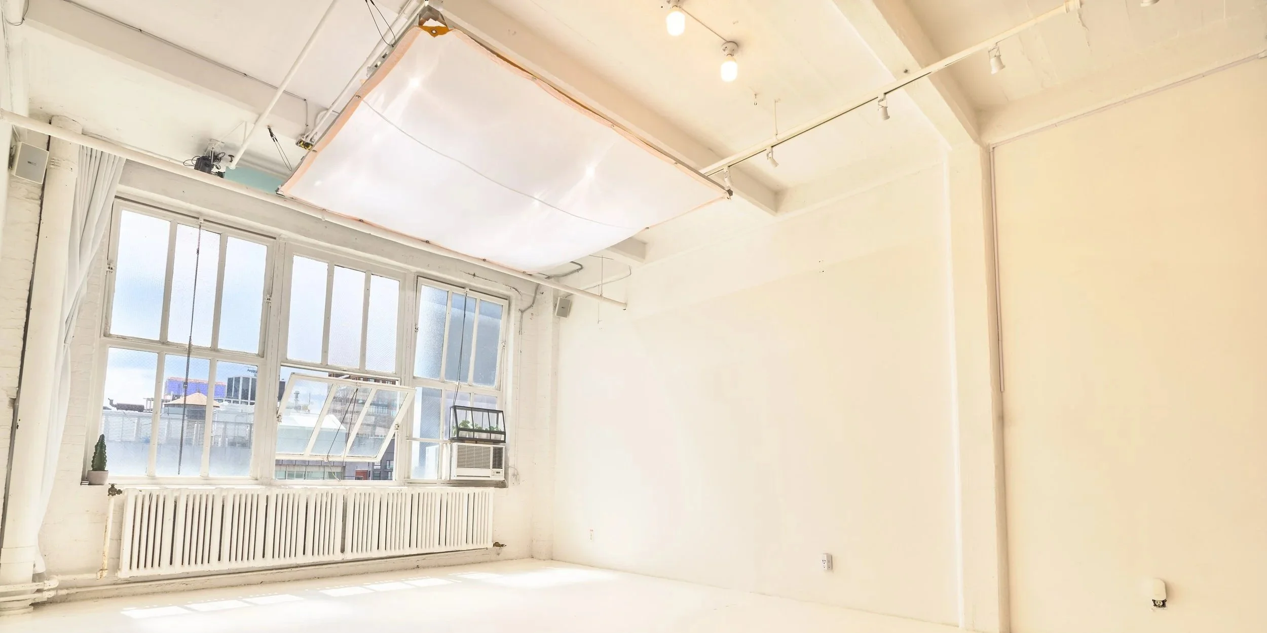 Bright room with large windows, a radiator under the windows, a small potted plant, and an air conditioning unit, with a large light fixture hanging from the ceiling.