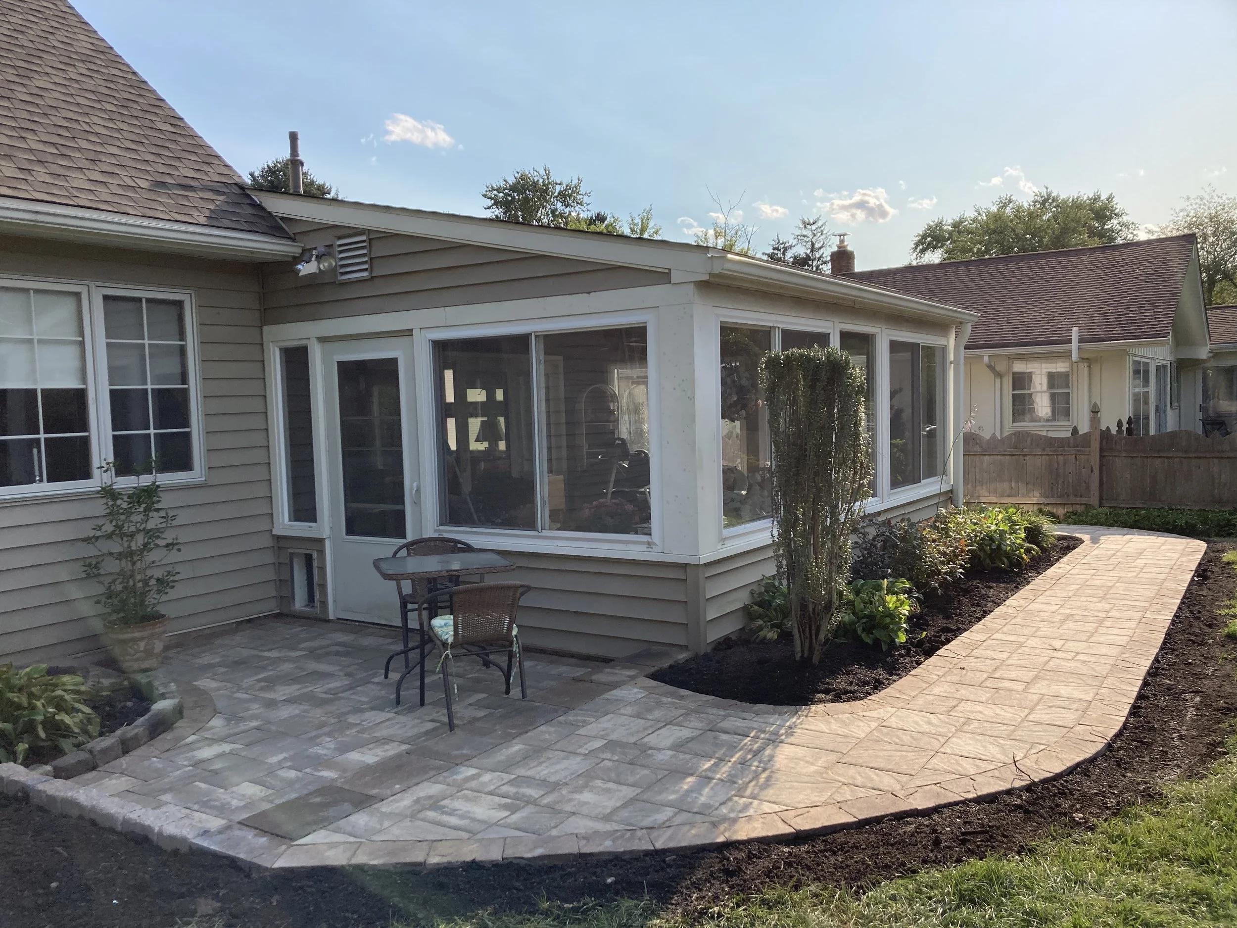 Newly constructed brick porch with outdoor table and chairs next to sunroom on backyard of house.