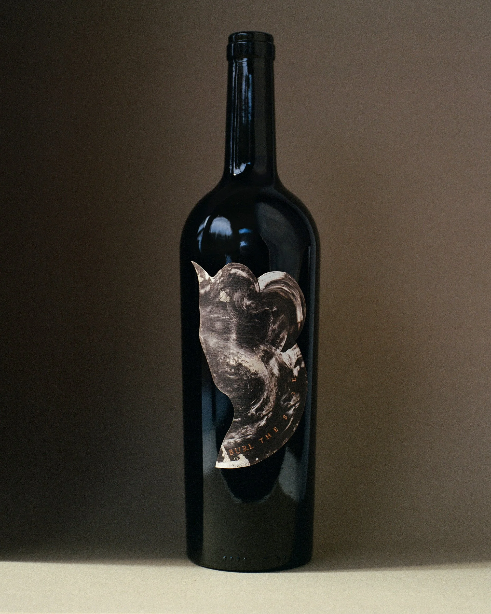 A dark wine bottle with an abstract label against a neutral background.