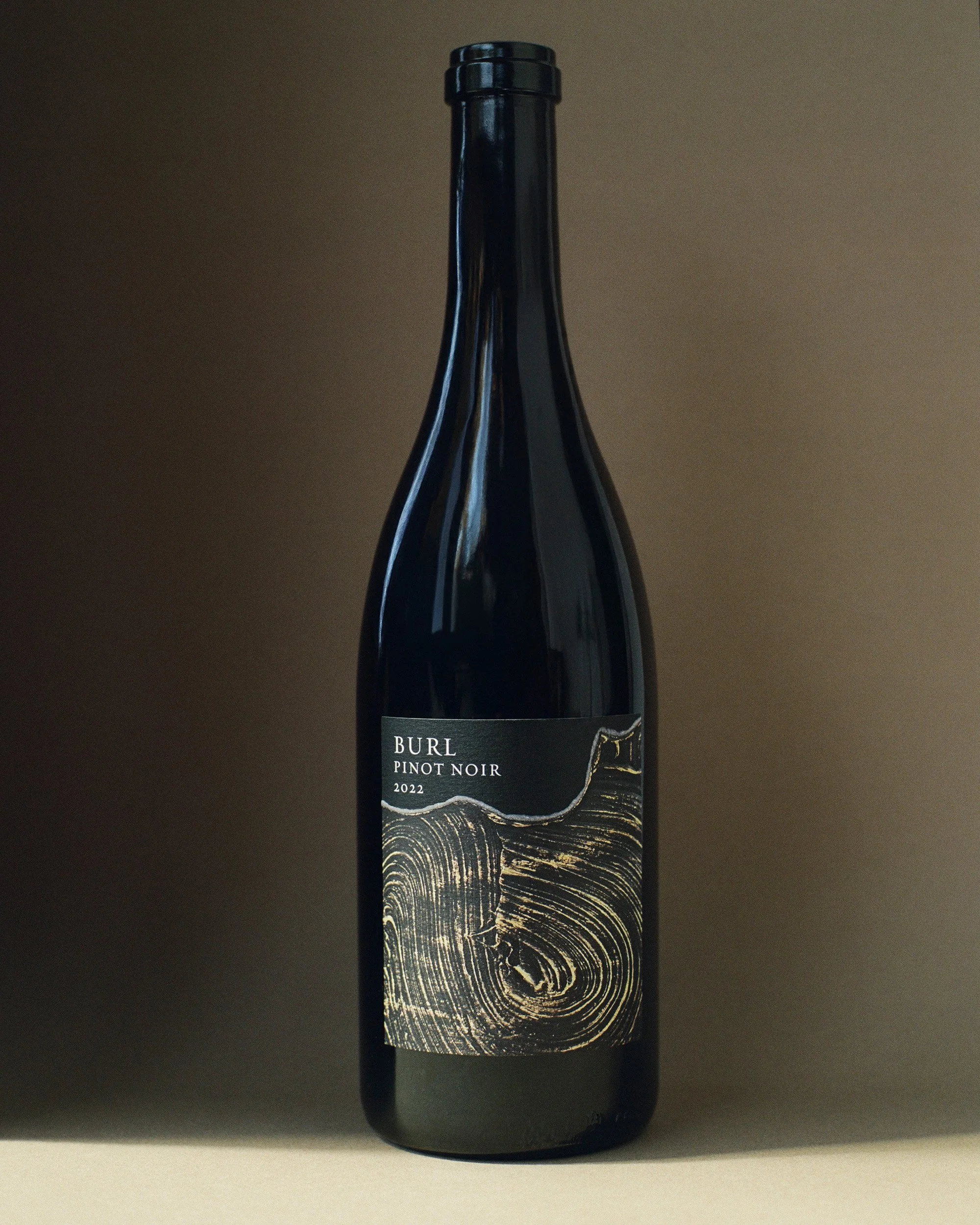 Bottle of Burl Pinot Noir 2022 with a textured label featuring wooden grain design, set against a neutral background.