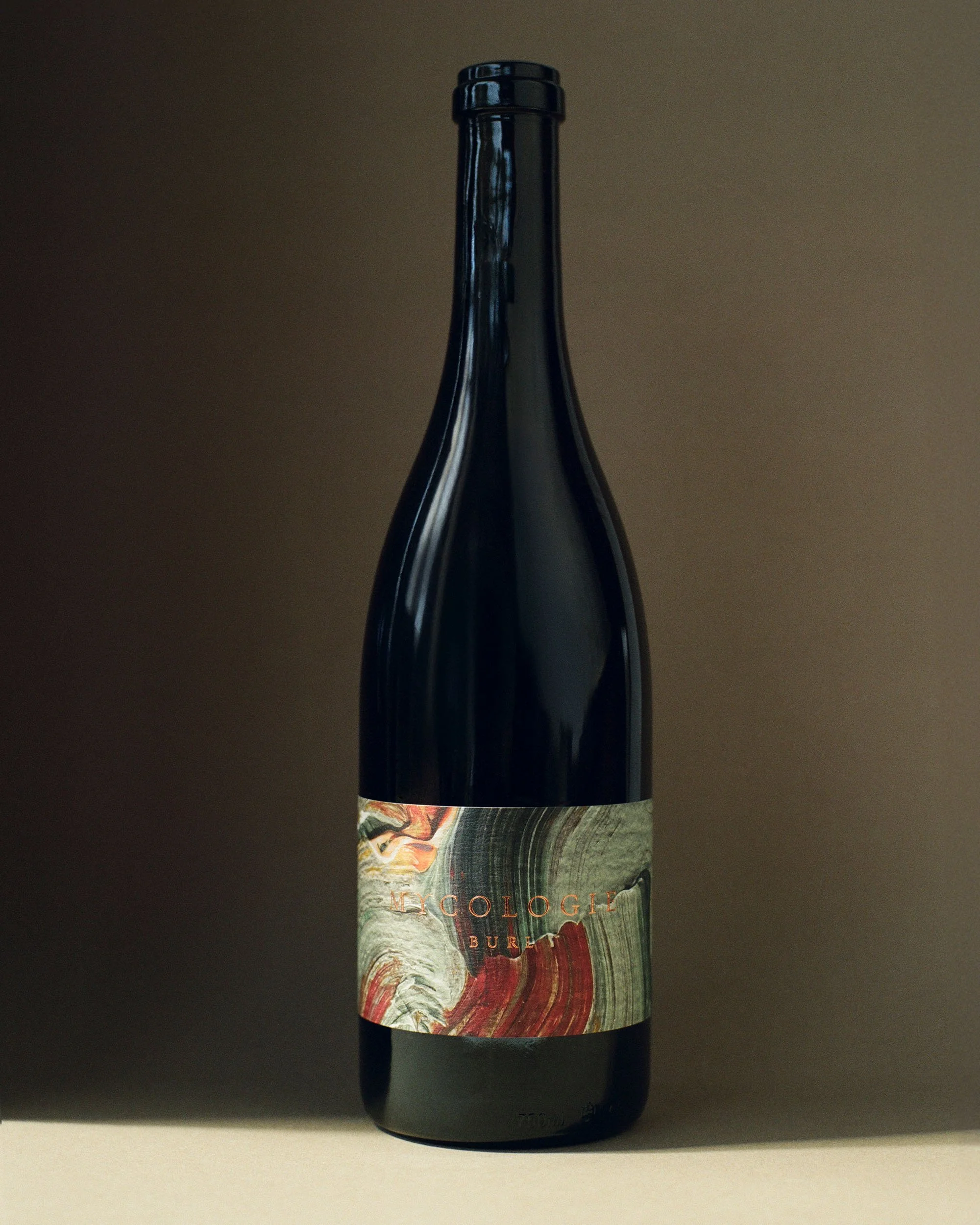A dark-colored wine bottle with a decorative label on a light brown background.
