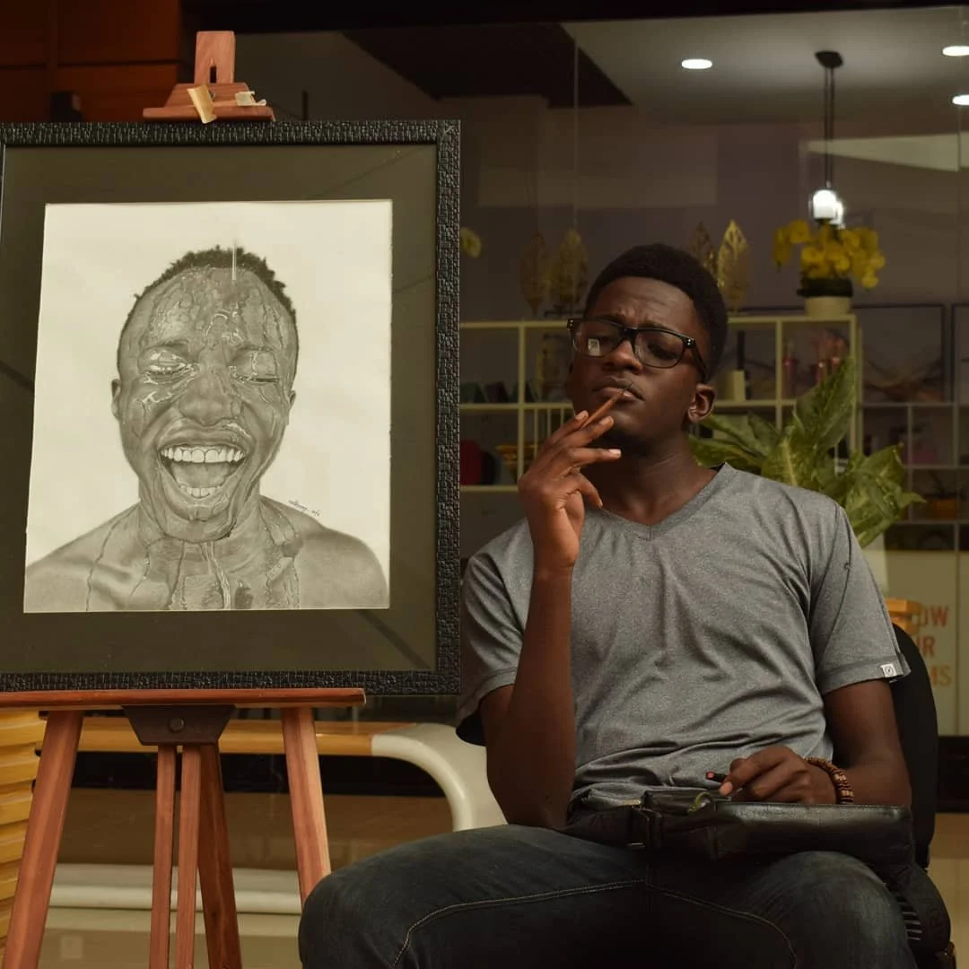 A young man in glasses sits with his hand on his chin next to a portrait of a woman with a wide, open-mouthed smile, drawn in black and white on an easel.